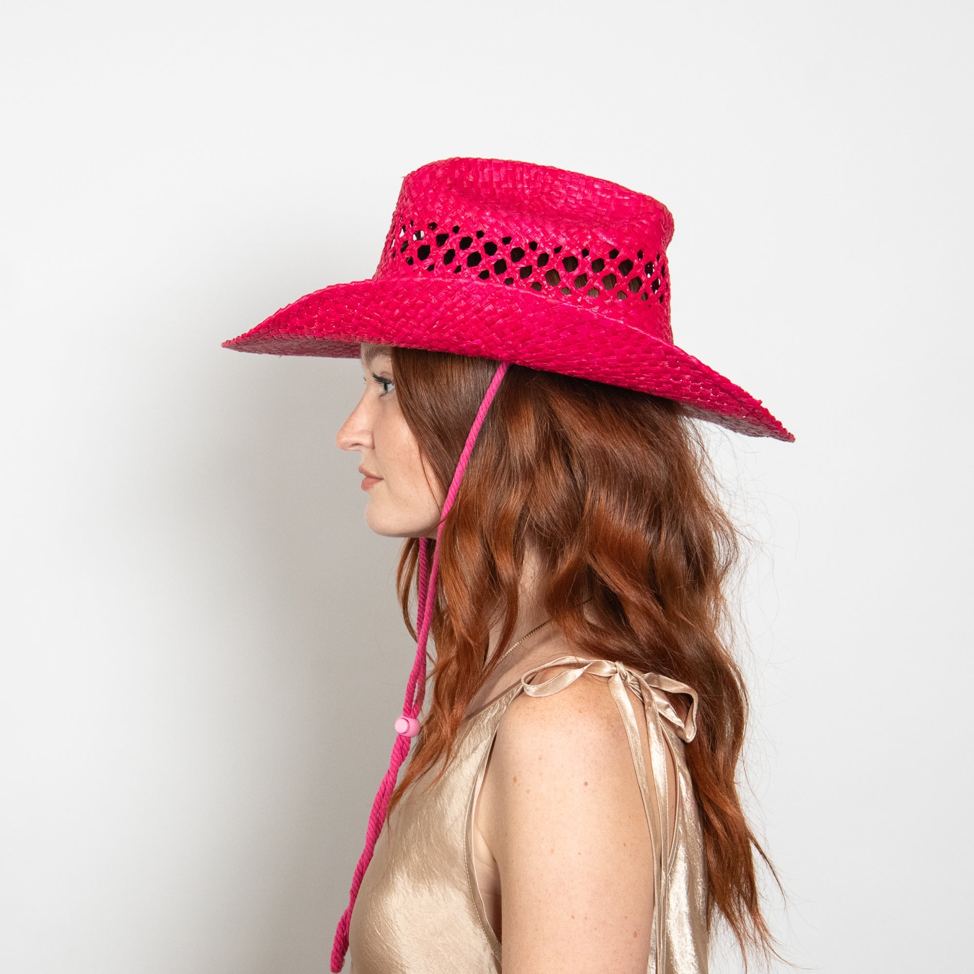 Woman wearing a bright pink sun hat on a light background