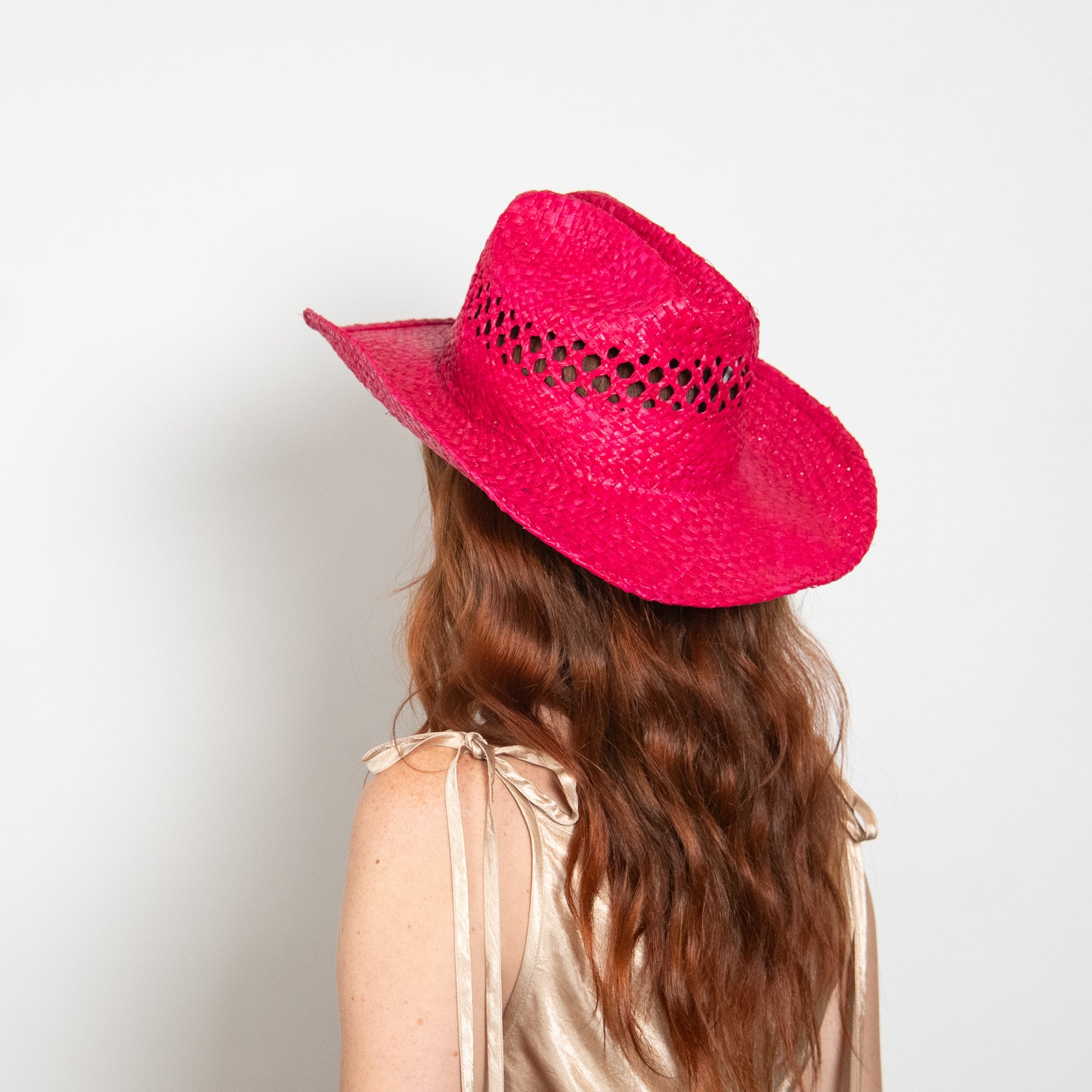 Person wearing a bright pink cowboy hat on a plain background