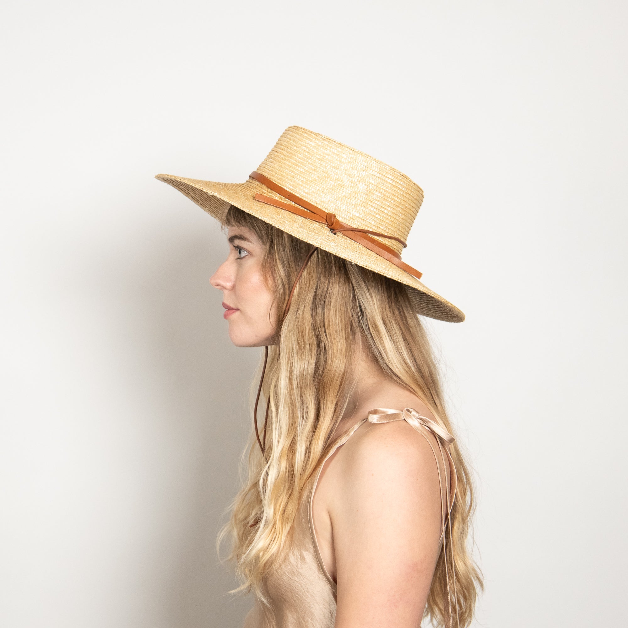 Woman wearing a straw hat with a brown ribbon on a plain background