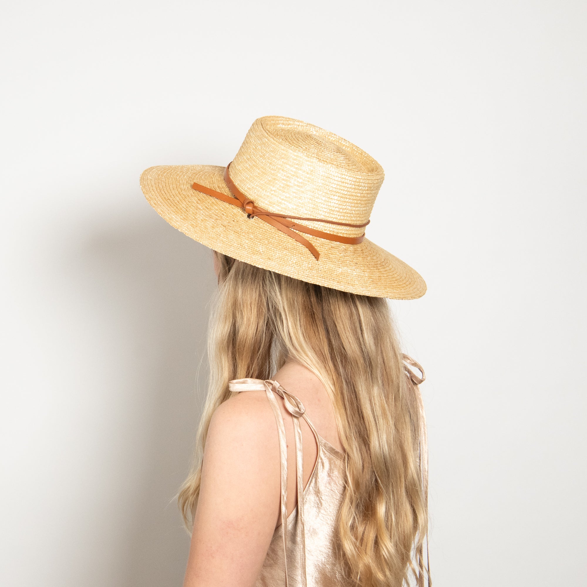 Person wearing a straw hat with a brown ribbon on a plain background