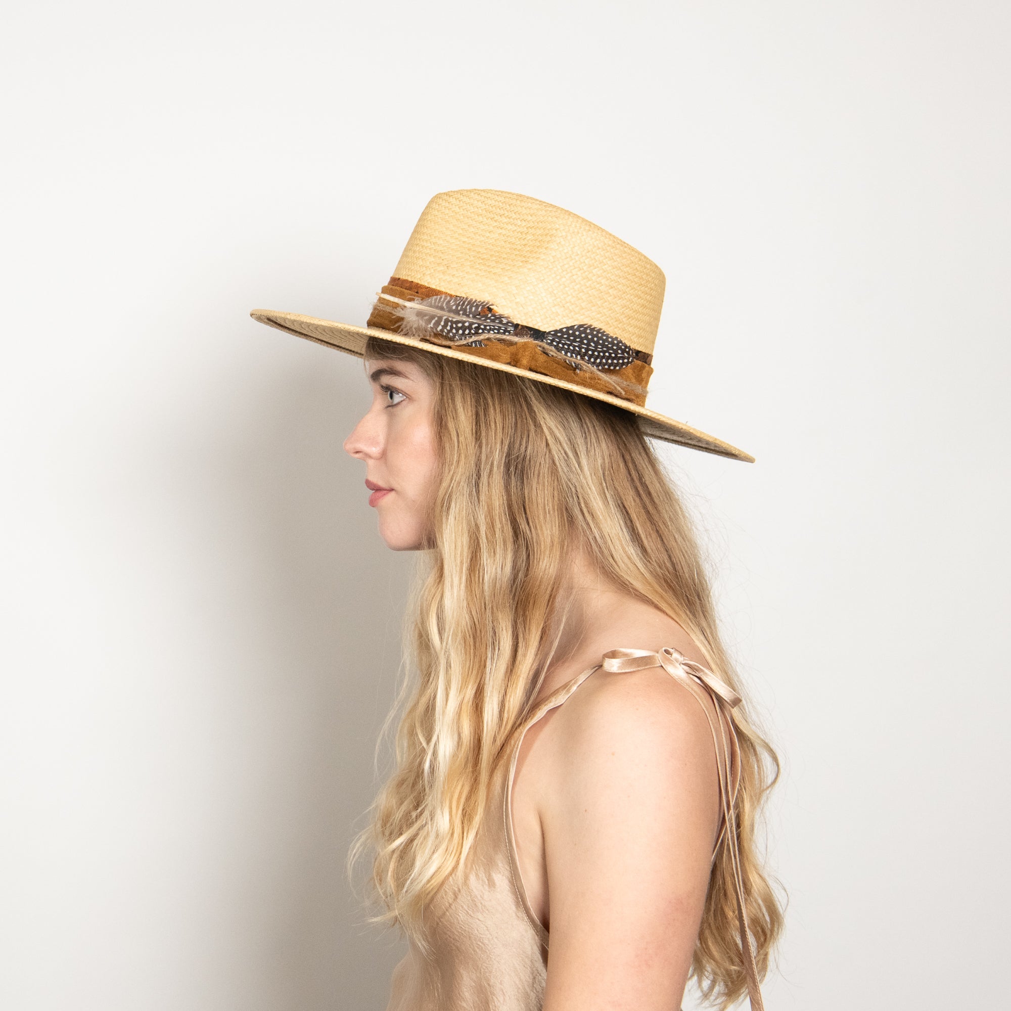 Woman wearing a straw hat with feather details on a plain background