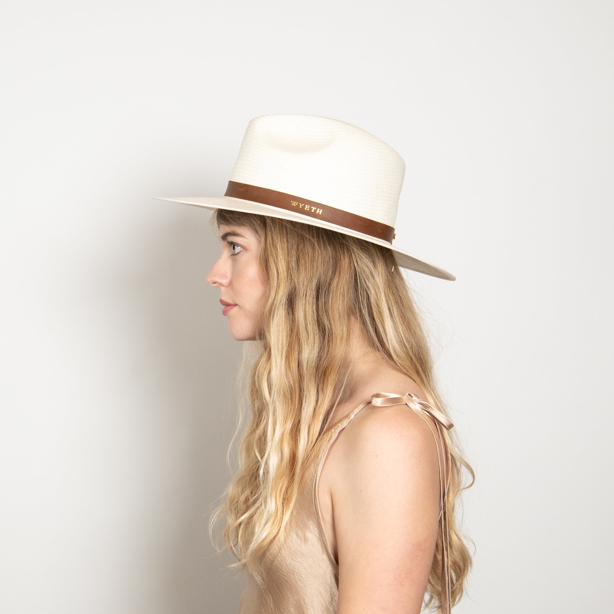 Woman wearing a white hat with a brown band on a light gray background