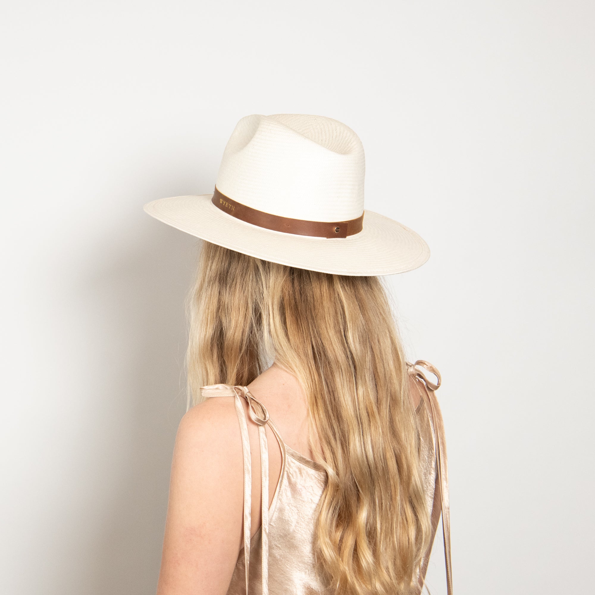 Person wearing a white hat with a brown band on a plain background