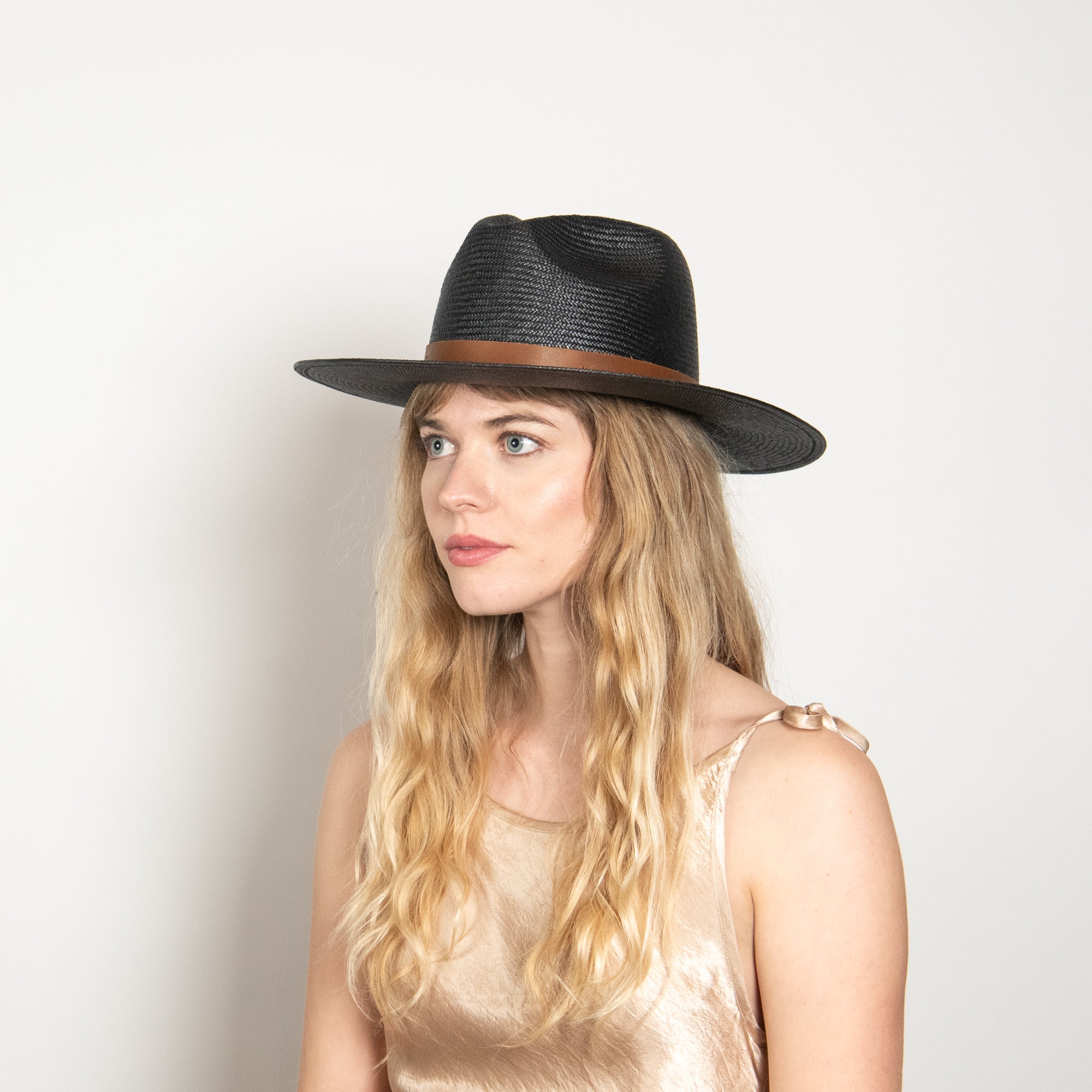 Woman wearing a black hat with a brown band on a plain background