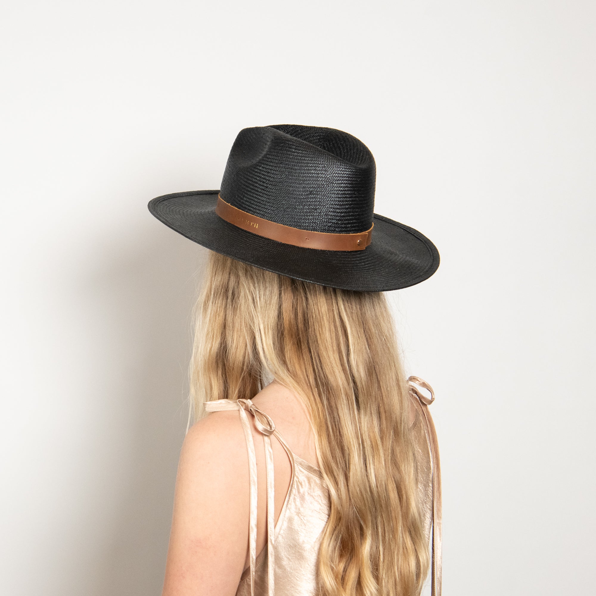 Person wearing a black hat with a brown band on a white background