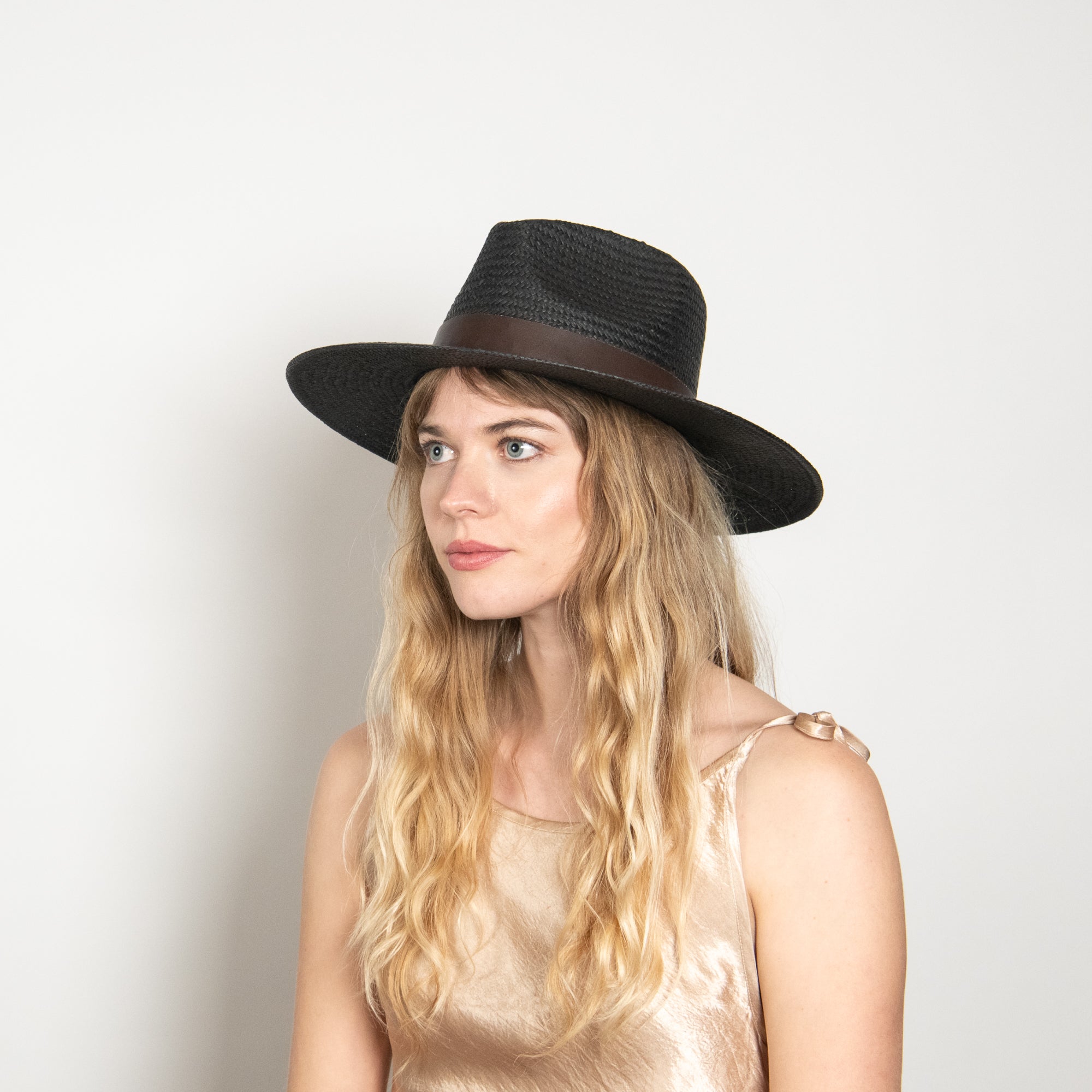 Woman wearing a black hat with a brown band on a plain background