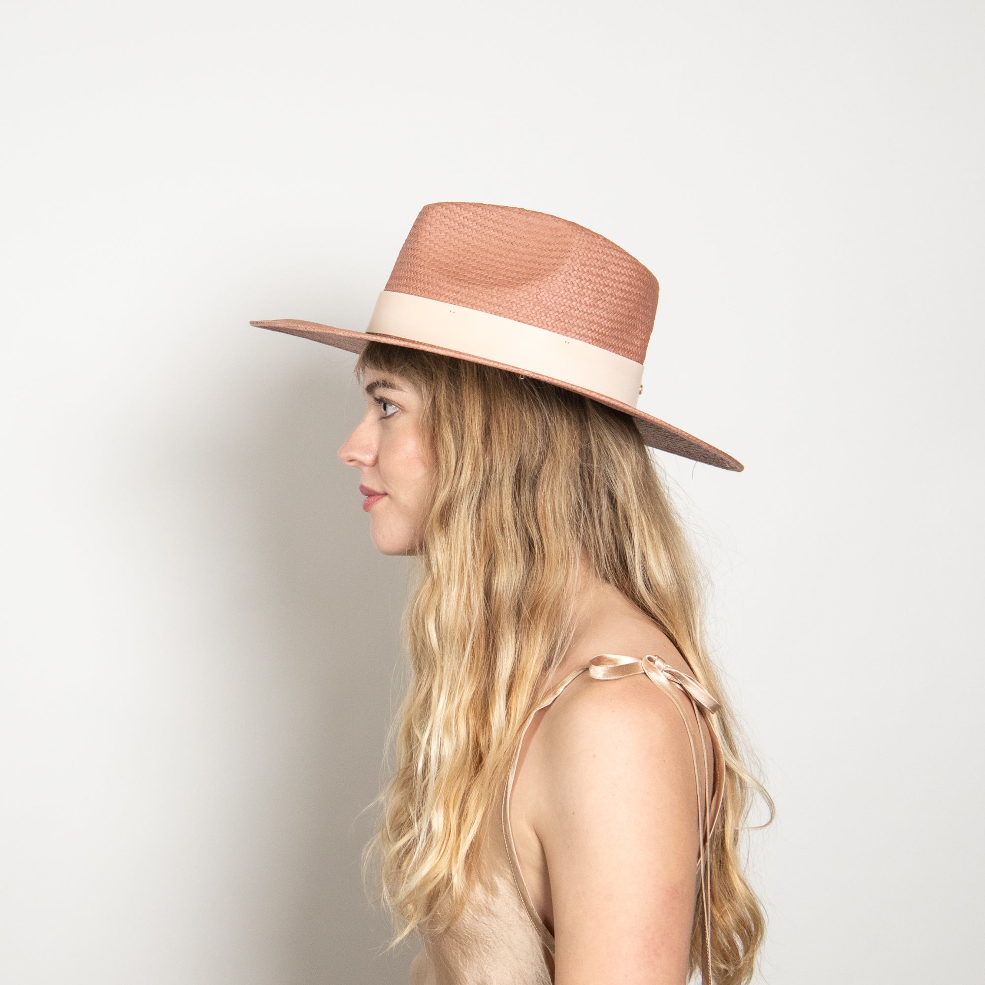 Woman wearing a pink straw hat against a plain background