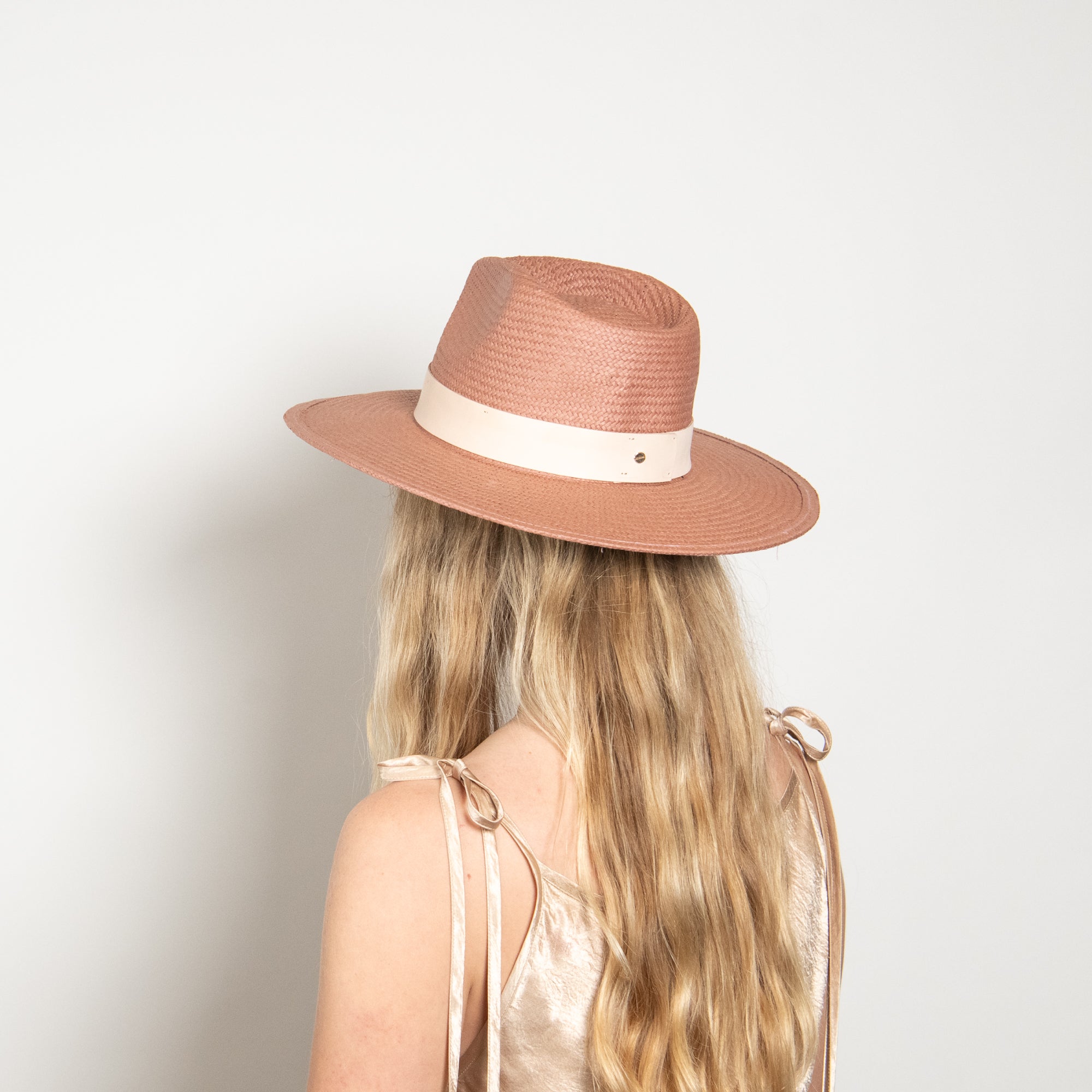 Person wearing a pink straw hat with a white band on a light gray background