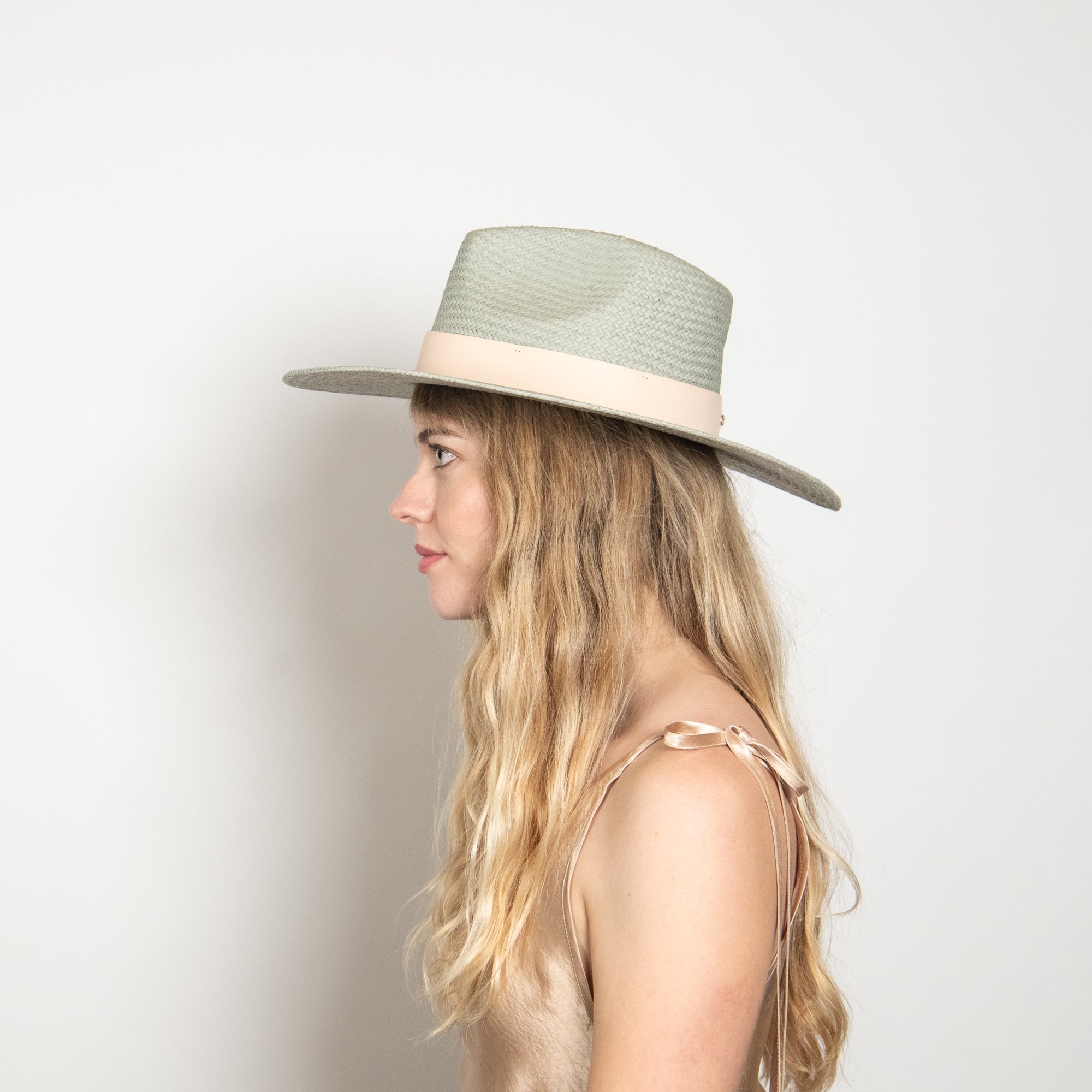 Woman wearing a light green fedora hat against a plain background