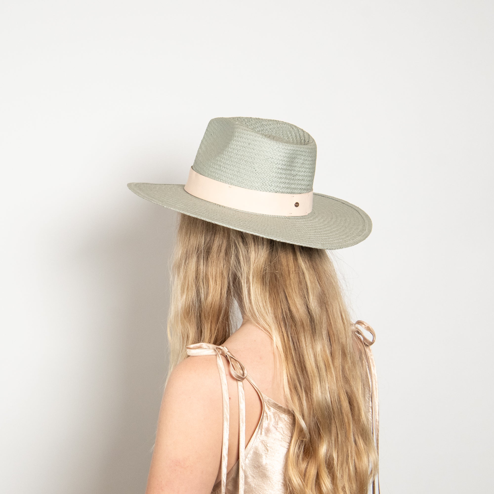 Person wearing a light green fedora hat with a beige band on a plain background