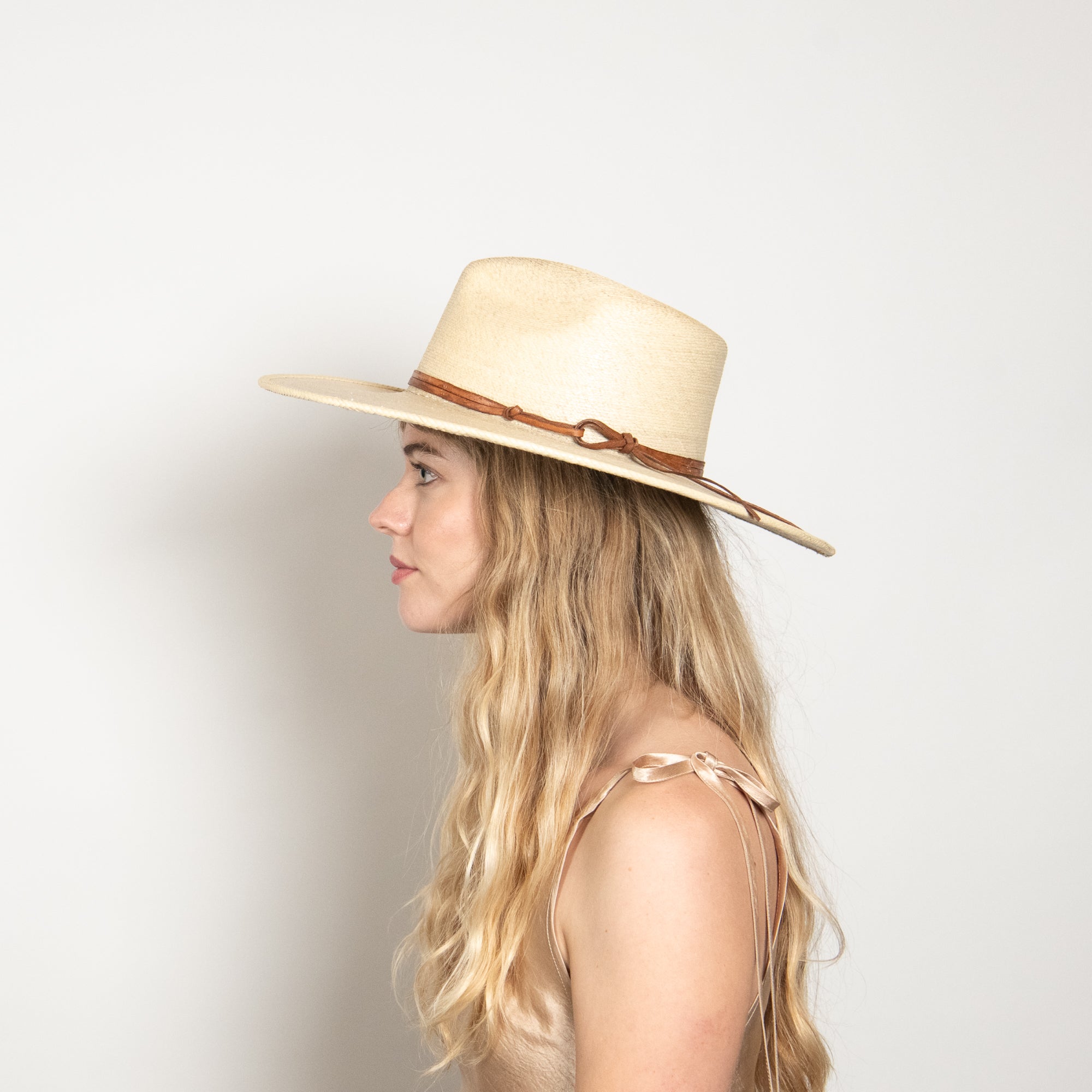 Woman wearing a beige hat with a brown band on a plain background