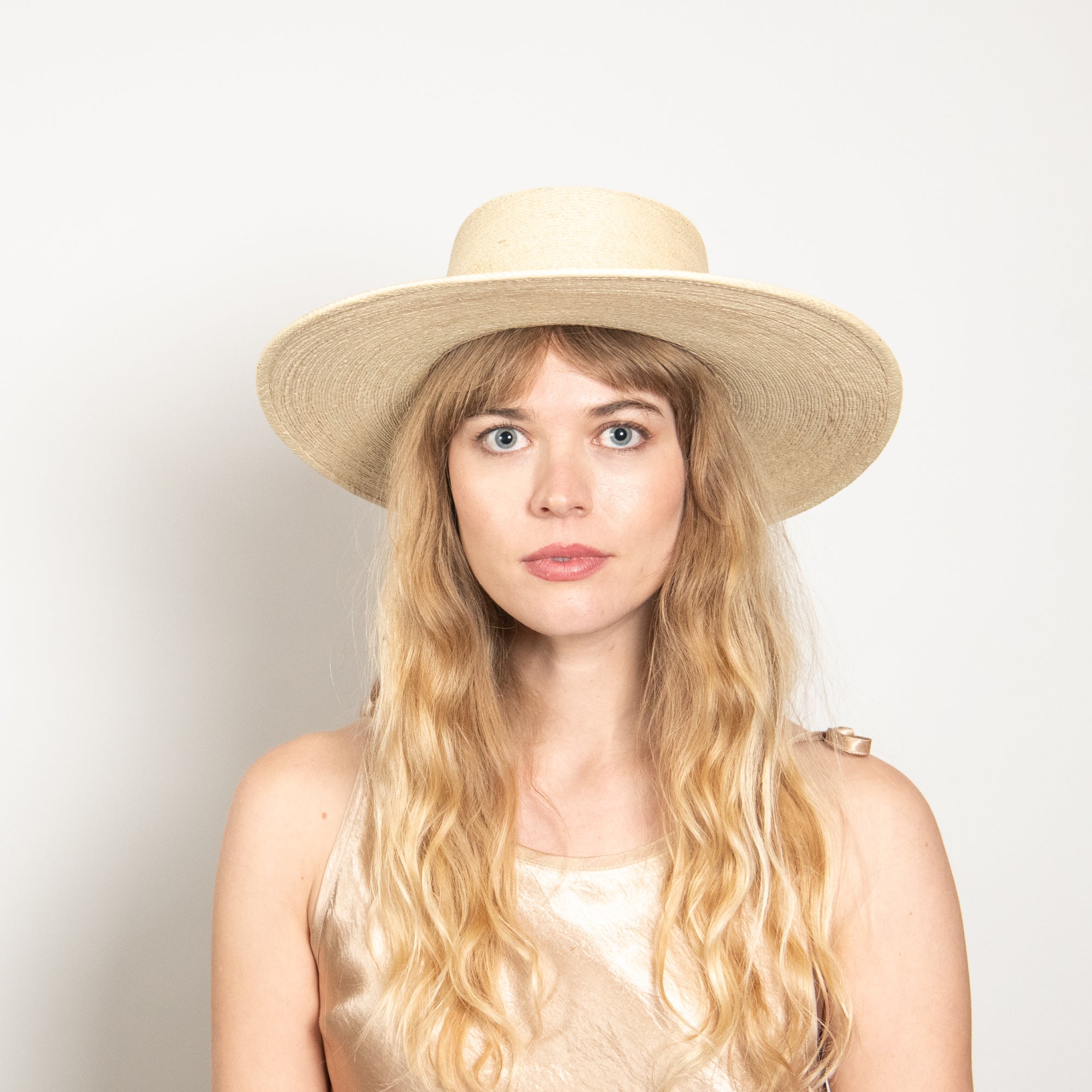 Woman wearing a wide-brimmed beige hat against a plain background