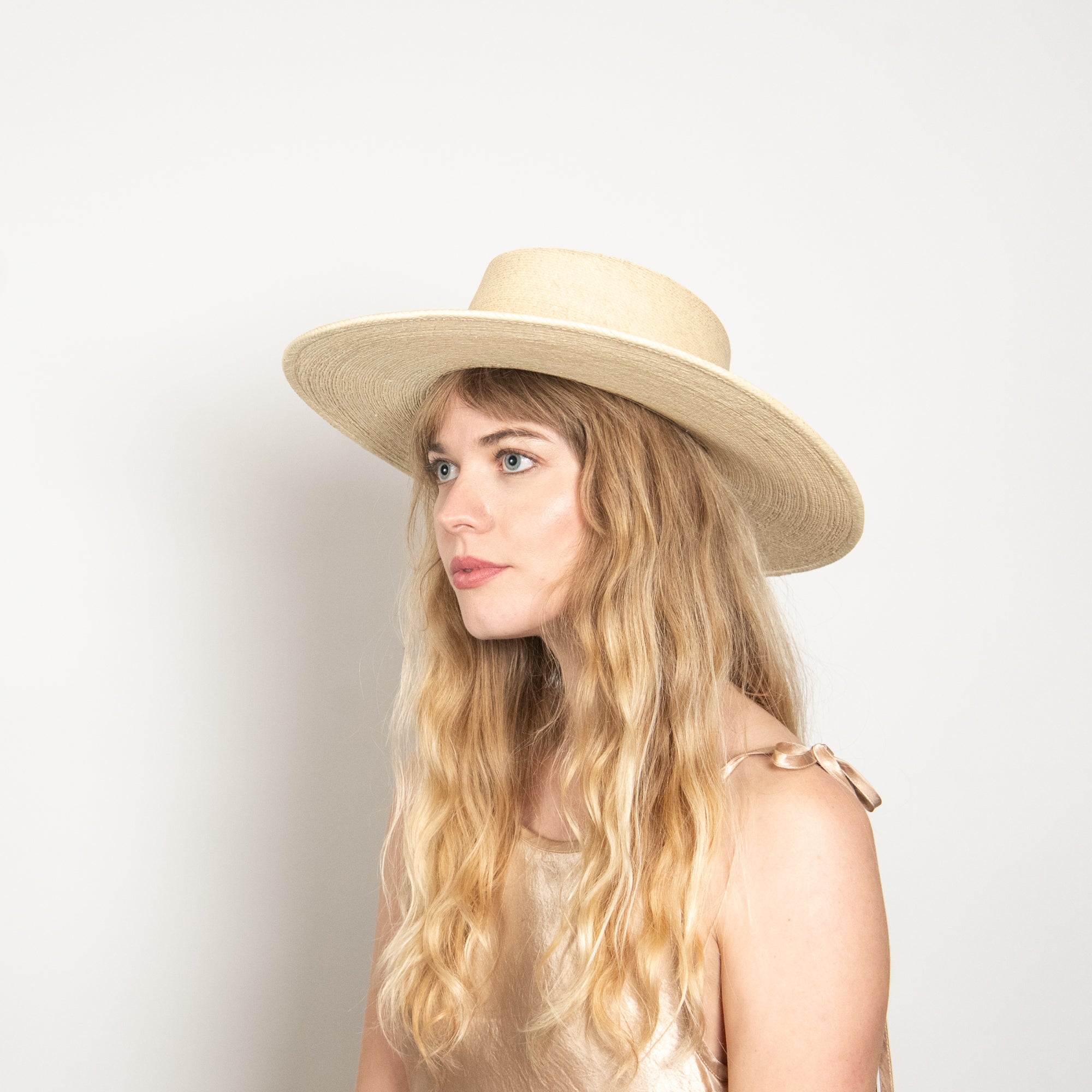 Woman wearing a wide-brimmed straw hat against a plain background