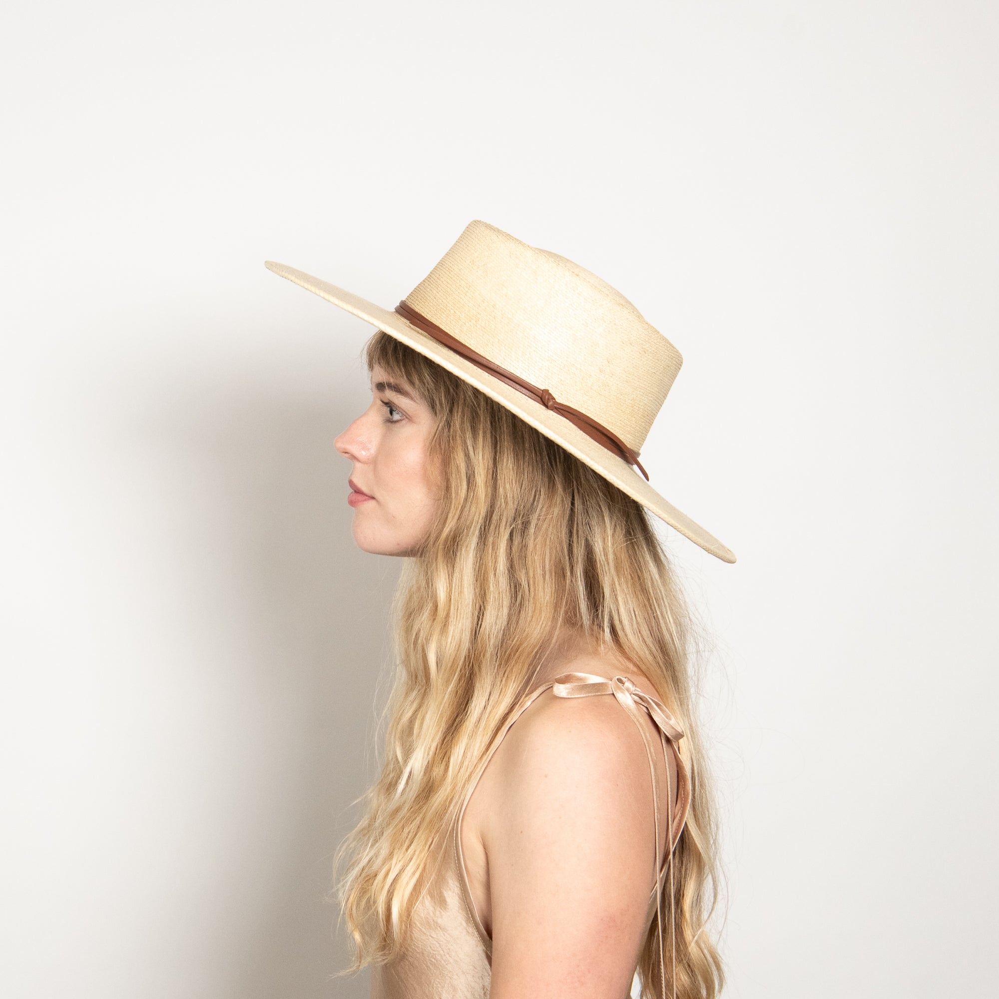 Woman wearing a beige straw hat with a brown band on a light background