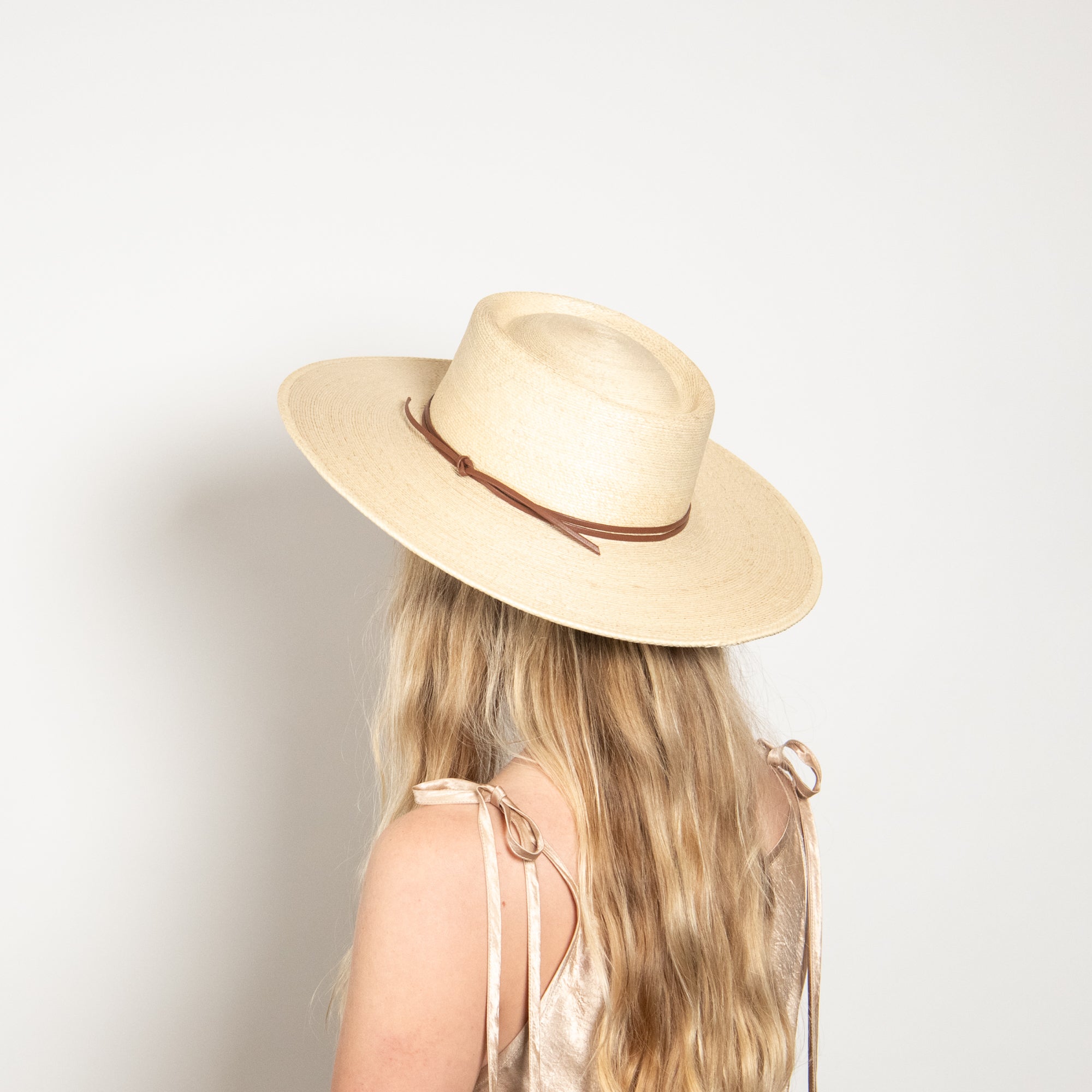 Person wearing a beige panama hat with a brown band on a plain background