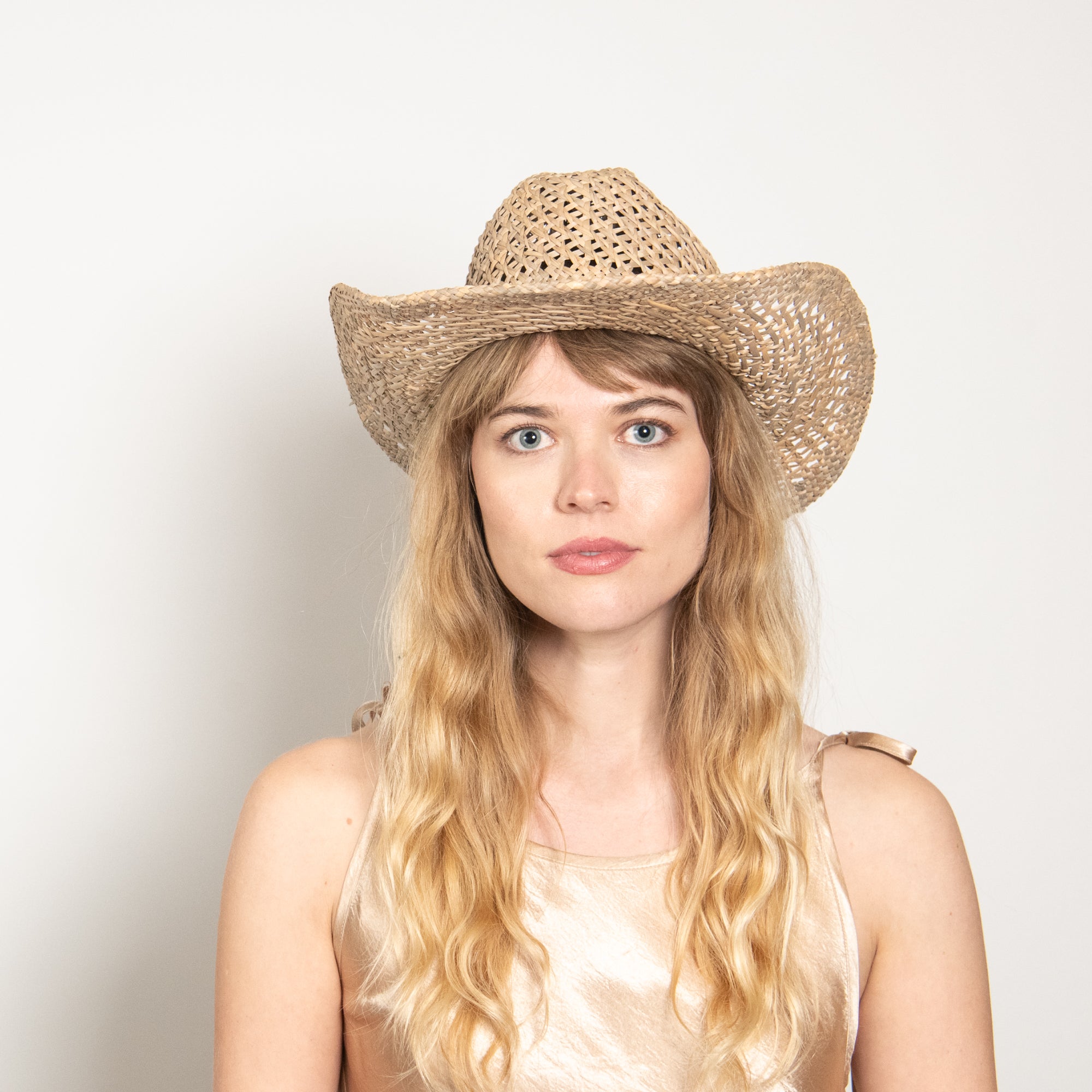 Woman wearing a straw cowboy hat against a plain background