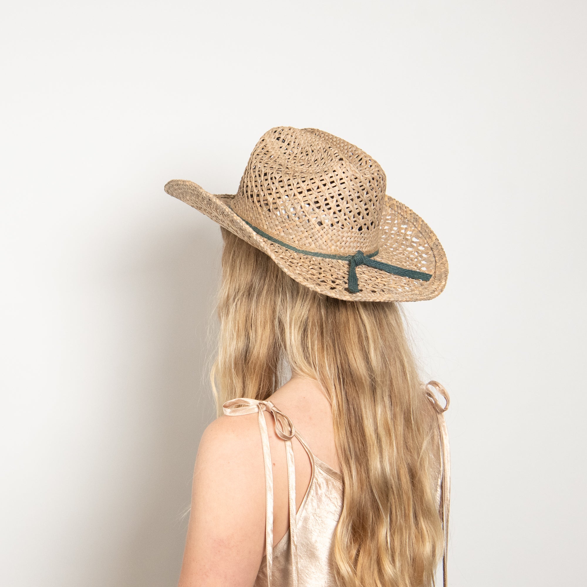 Person wearing a straw hat with a green ribbon on a plain background