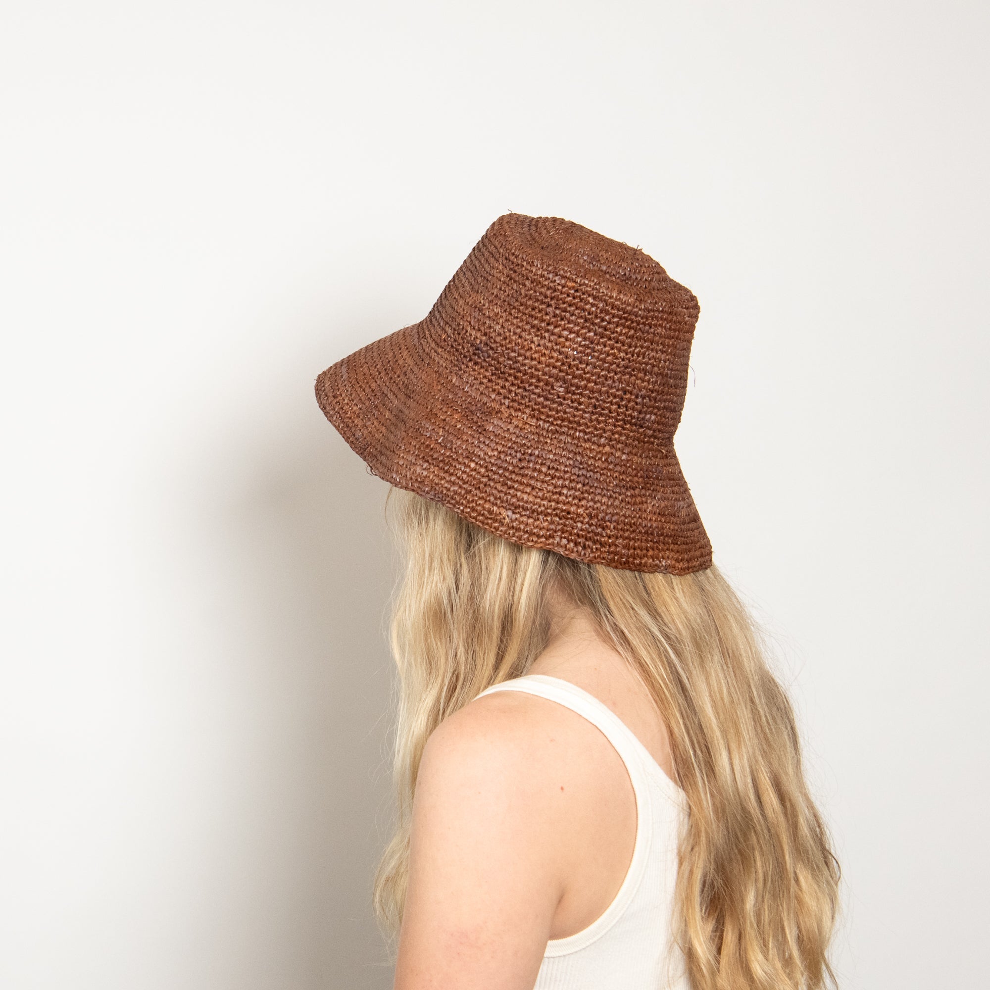 Brown woven bucket hat worn by a person on a plain background