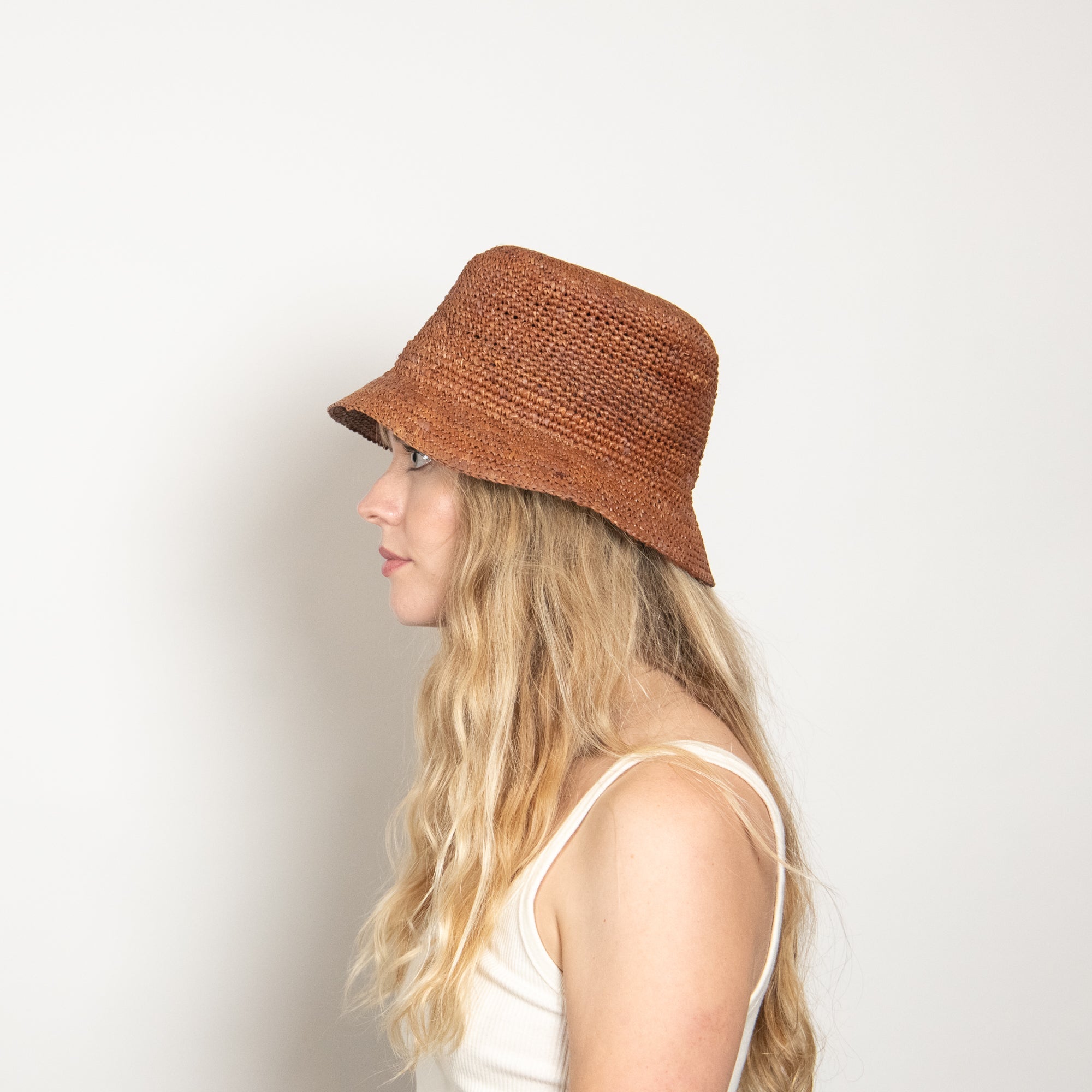 Woman wearing a brown woven bucket hat on a plain background