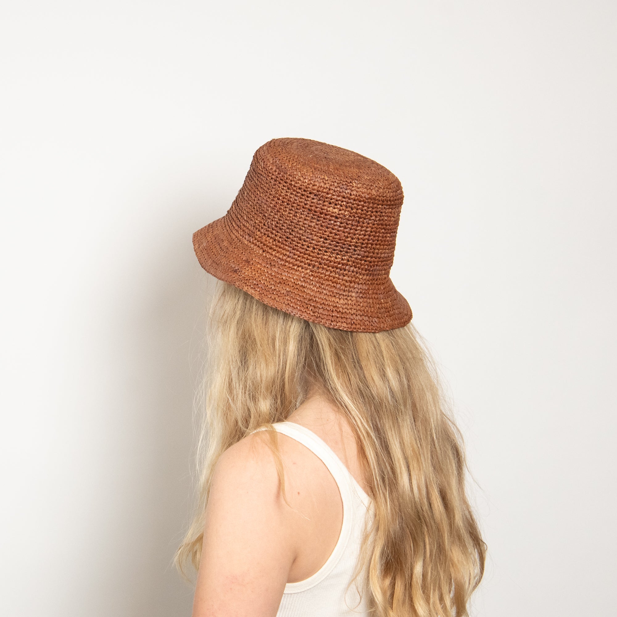 Person wearing a brown woven bucket hat on a plain background