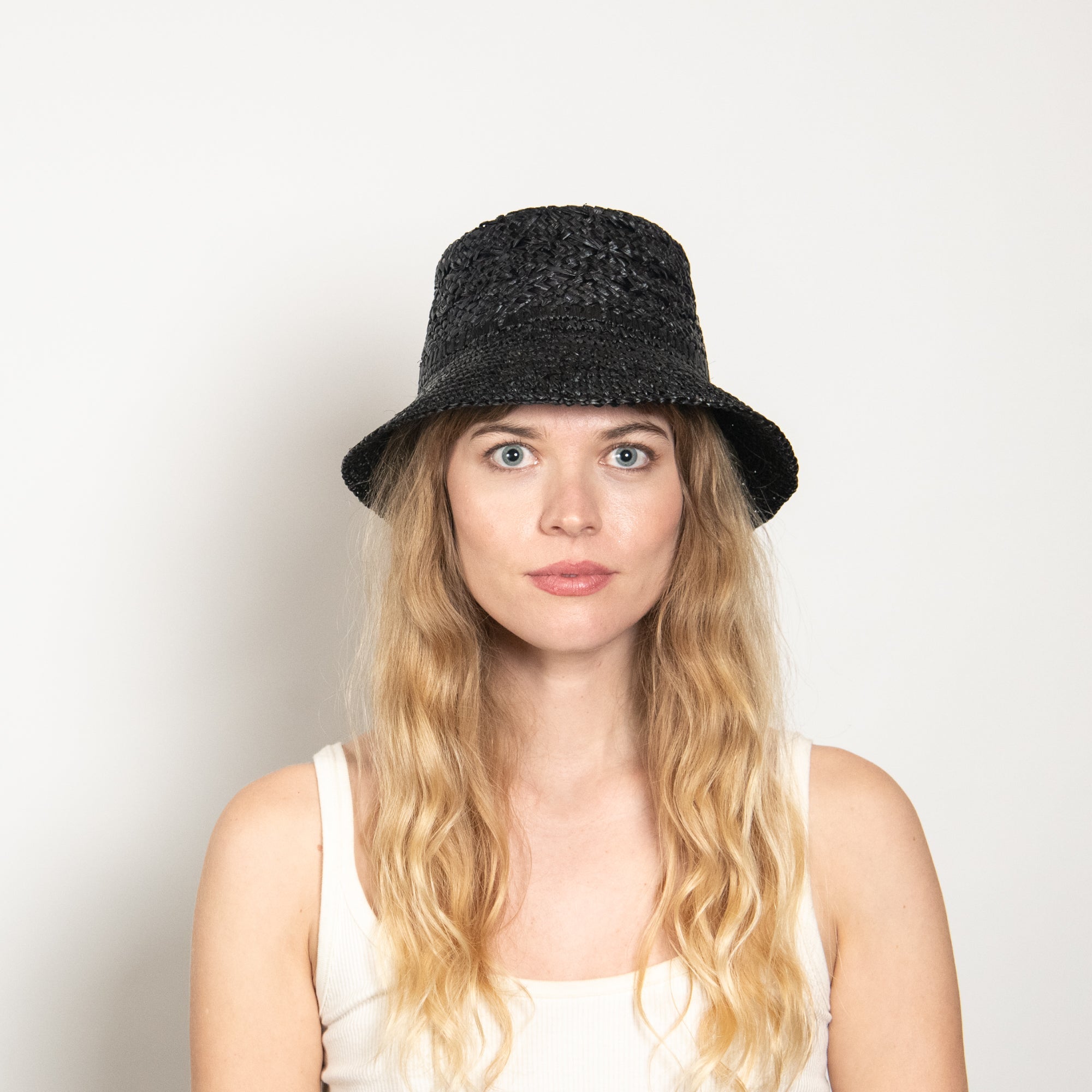 Woman wearing a black woven hat against a plain background