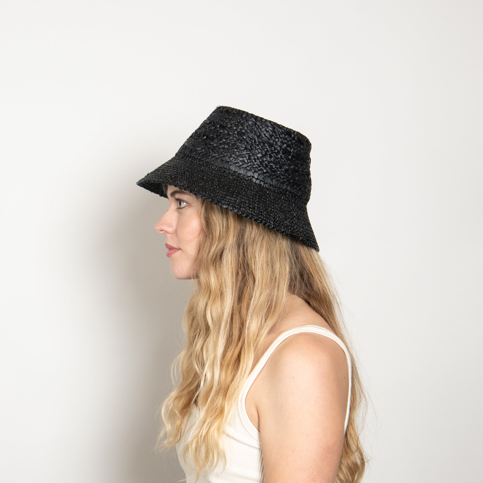 Woman wearing a black woven hat against a plain background