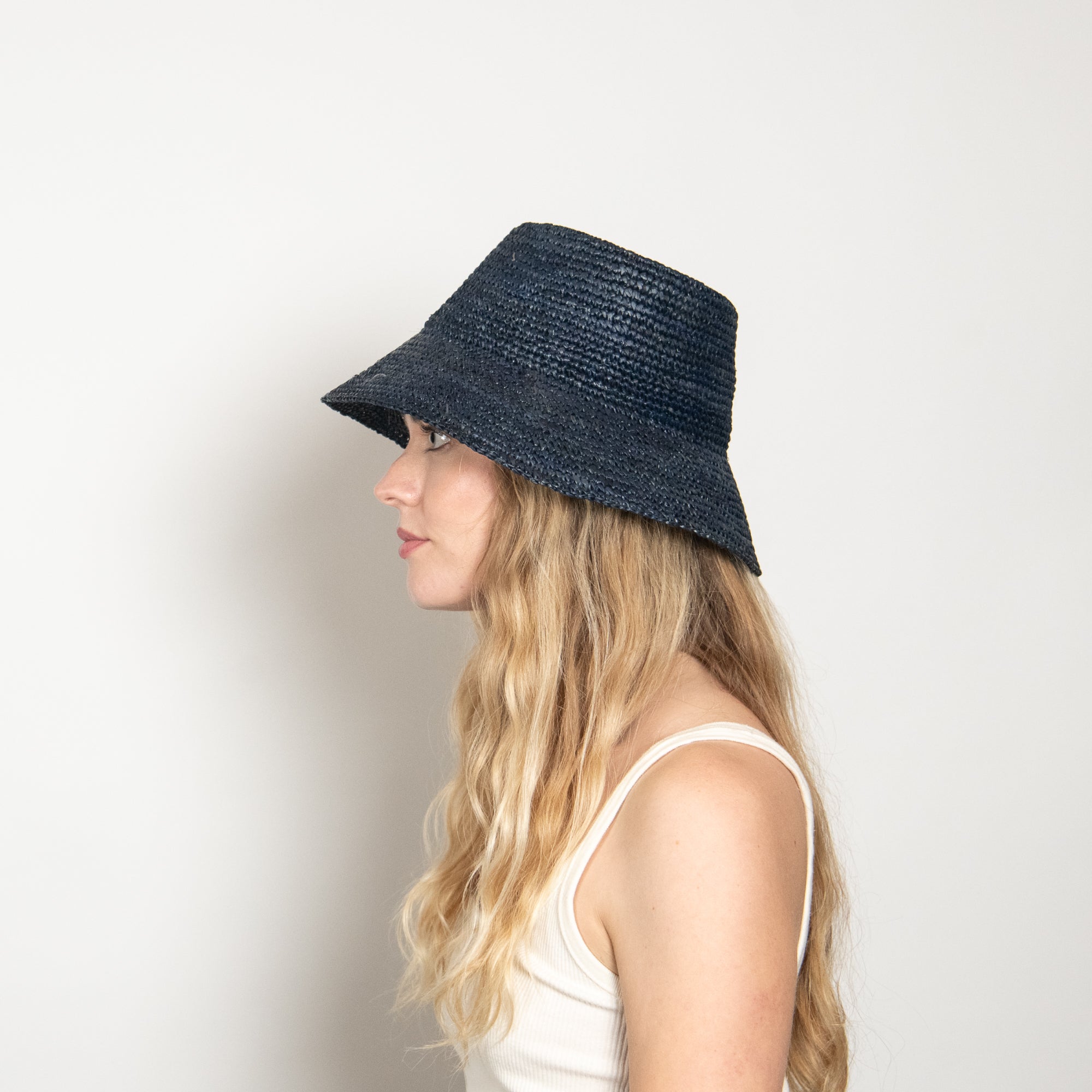 Woman wearing a navy blue straw hat on a light gray background