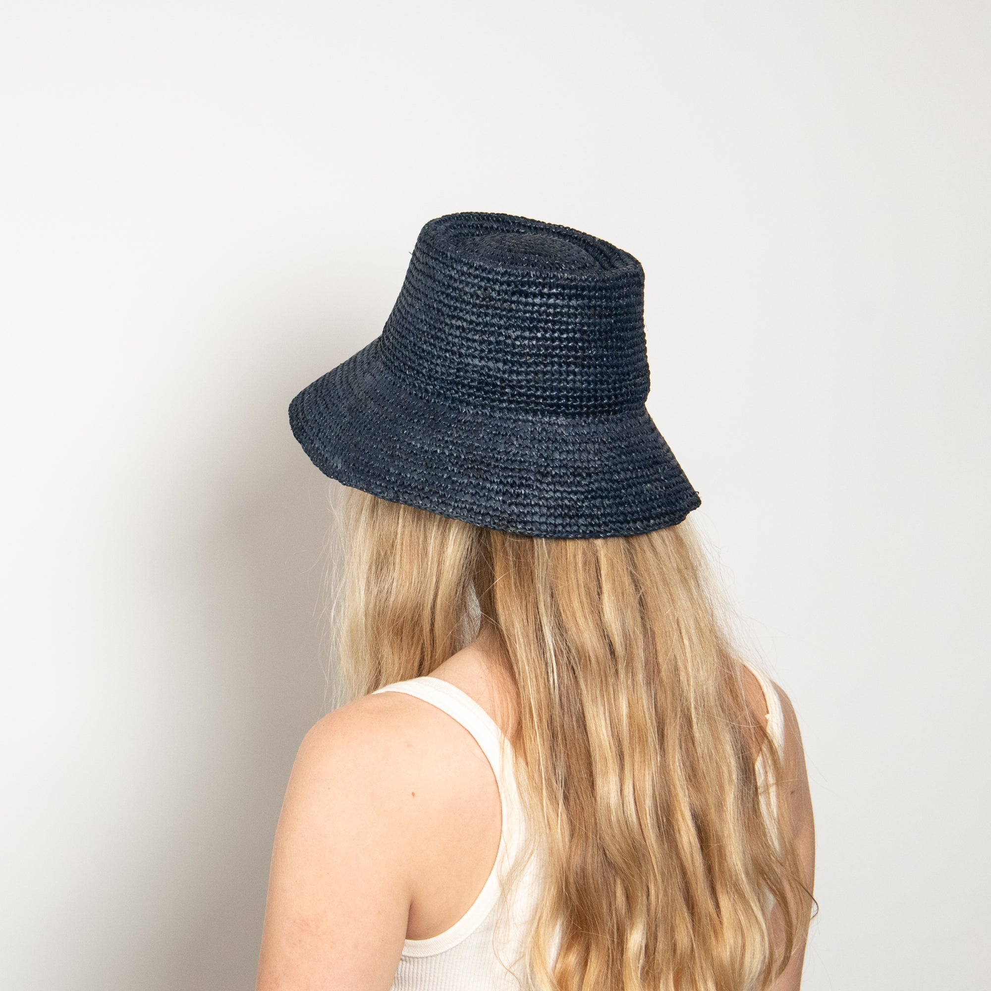 Person wearing a navy blue straw hat on a plain background
