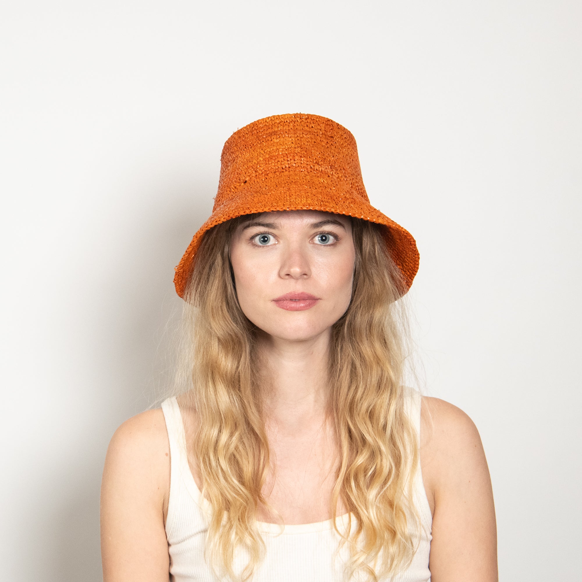 Woman wearing an orange bucket hat against a plain background