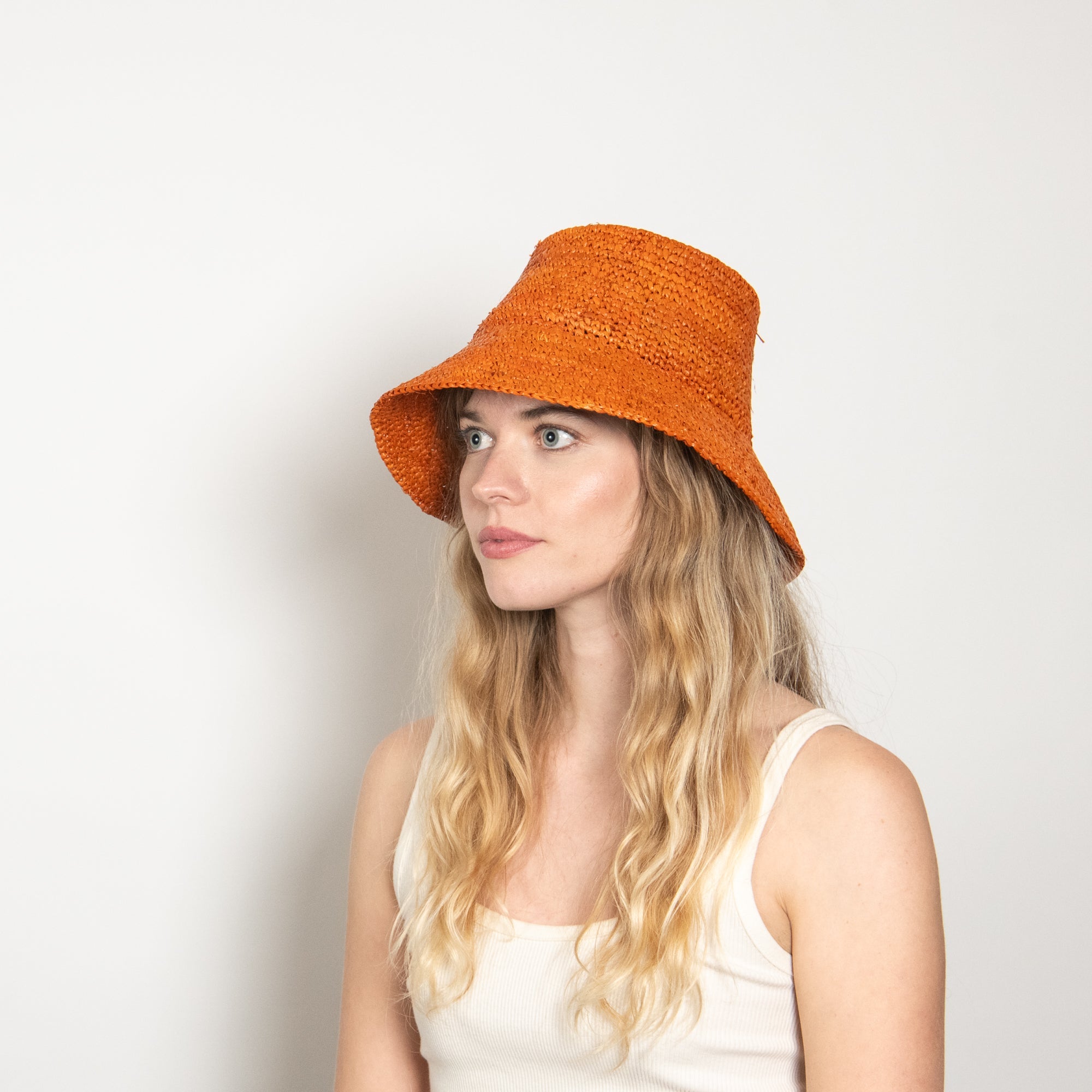 Woman wearing an orange bucket hat against a plain background