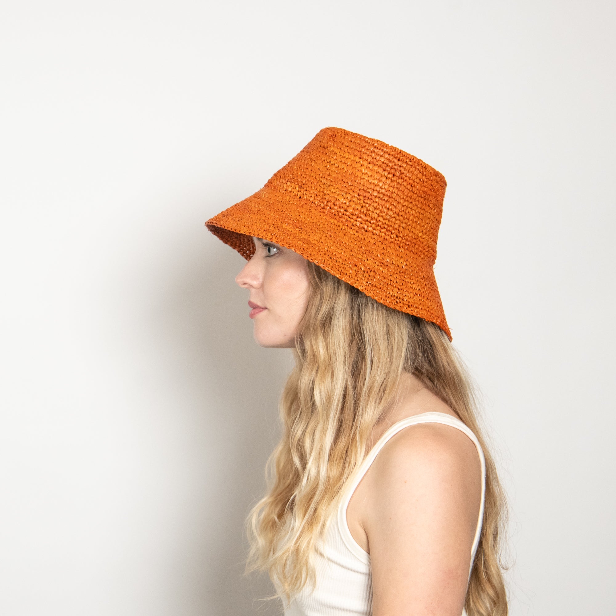 Woman wearing an orange woven hat against a plain background