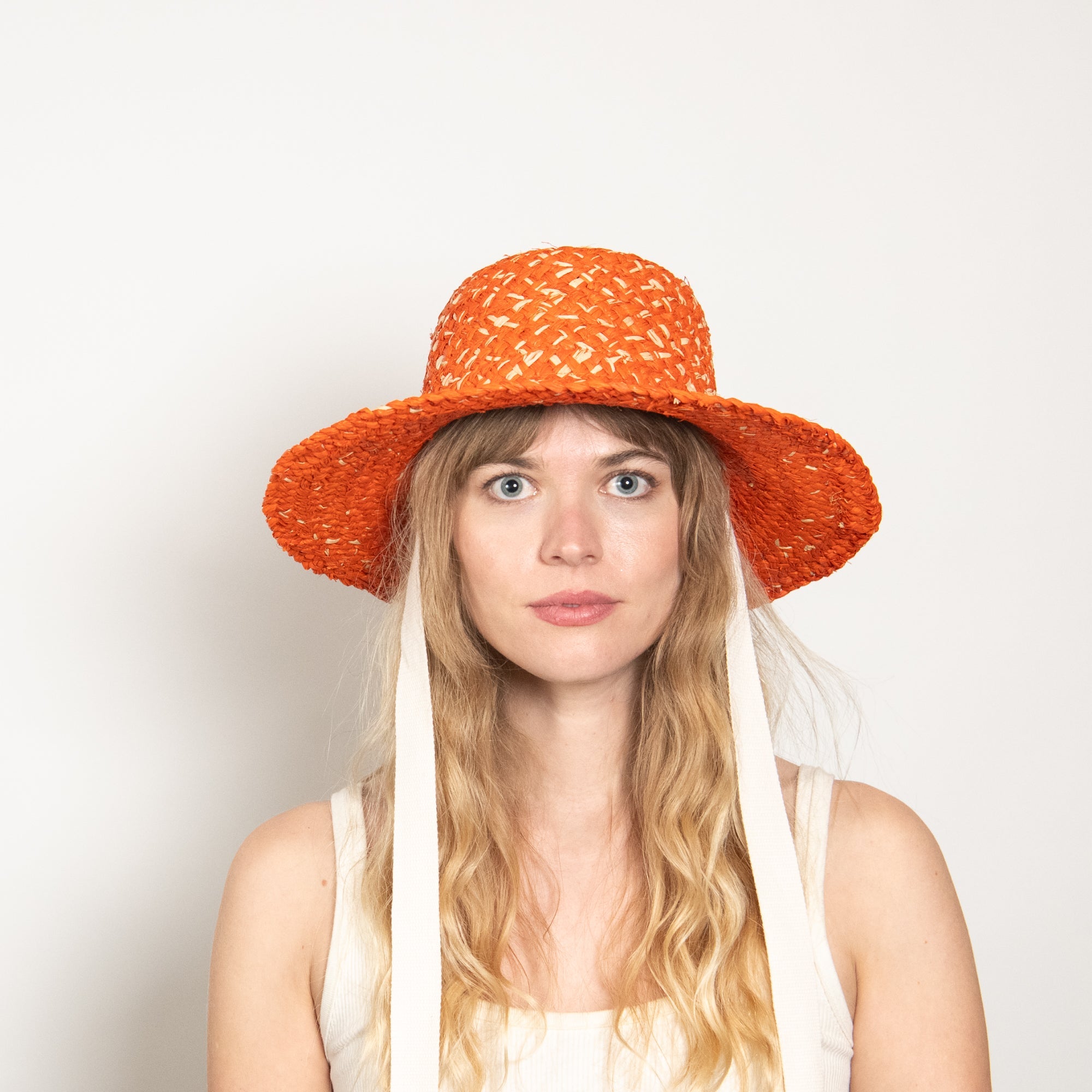 Woman wearing an orange straw hat against a plain background