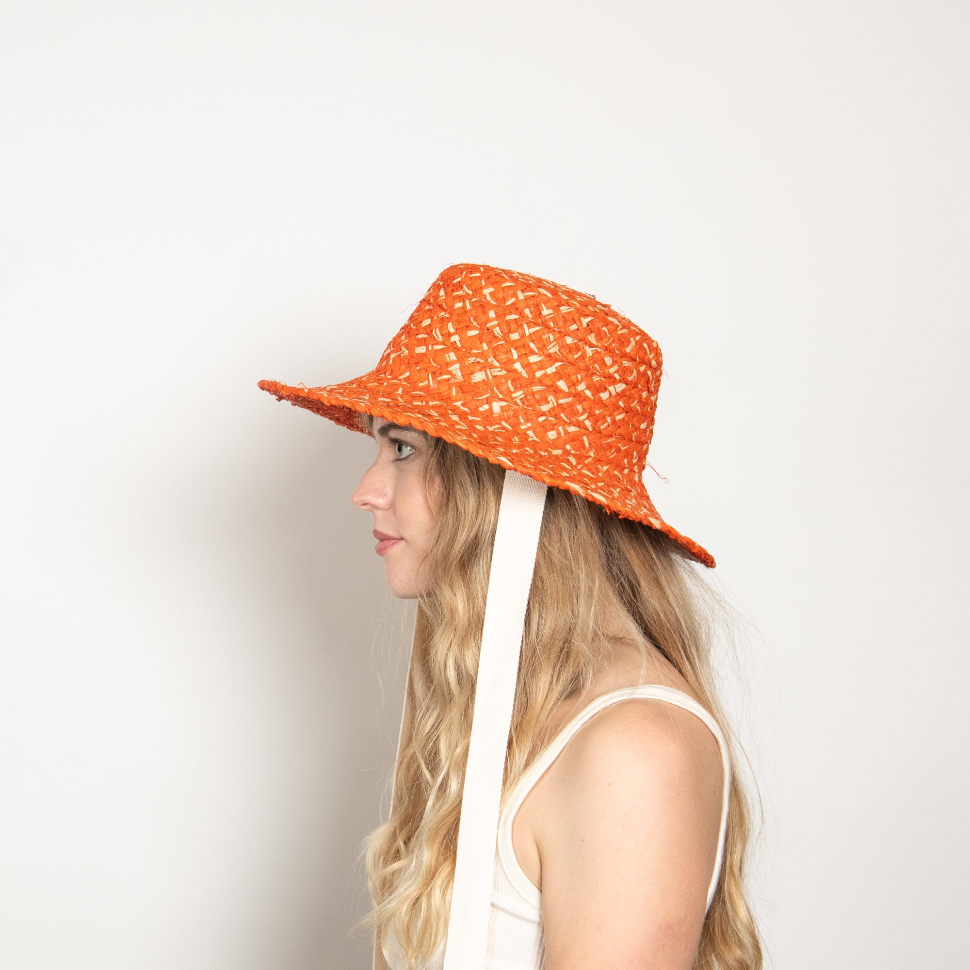 Person wearing an orange patterned sun hat with a white strap on a light background