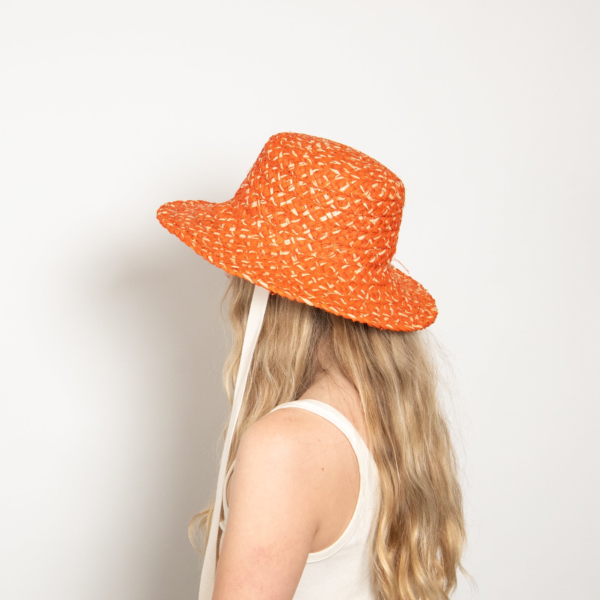 Orange patterned sun hat worn by a person on a plain background