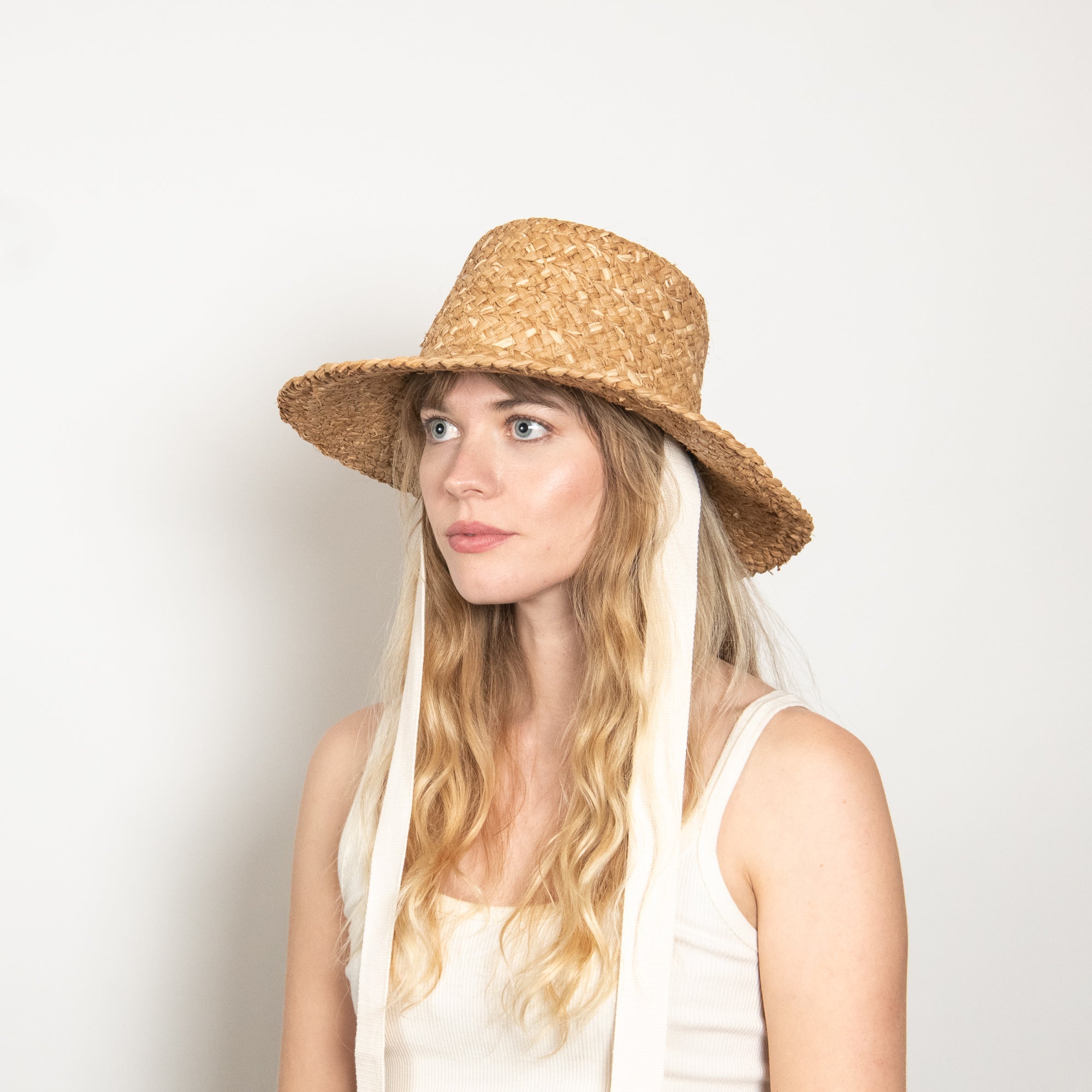 Woman wearing a straw hat and white scarf against a plain background