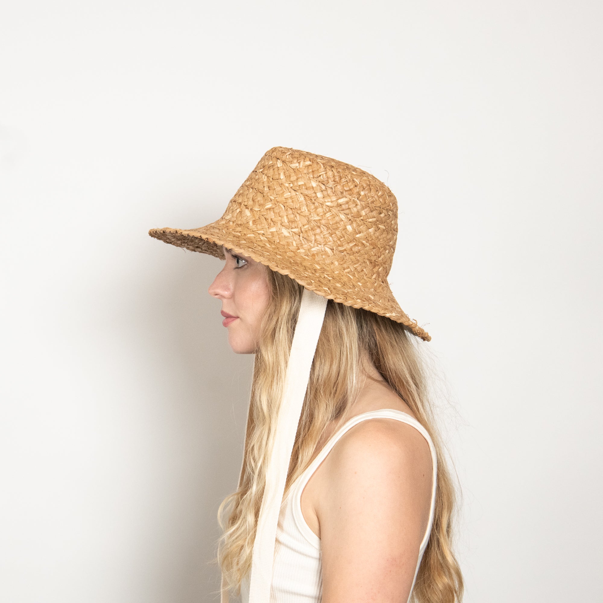 Woman wearing a straw hat with a white strap on a light background