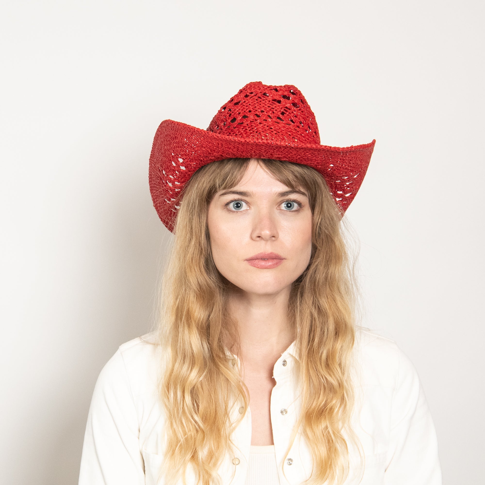 Woman wearing a red cowboy hat against a plain background