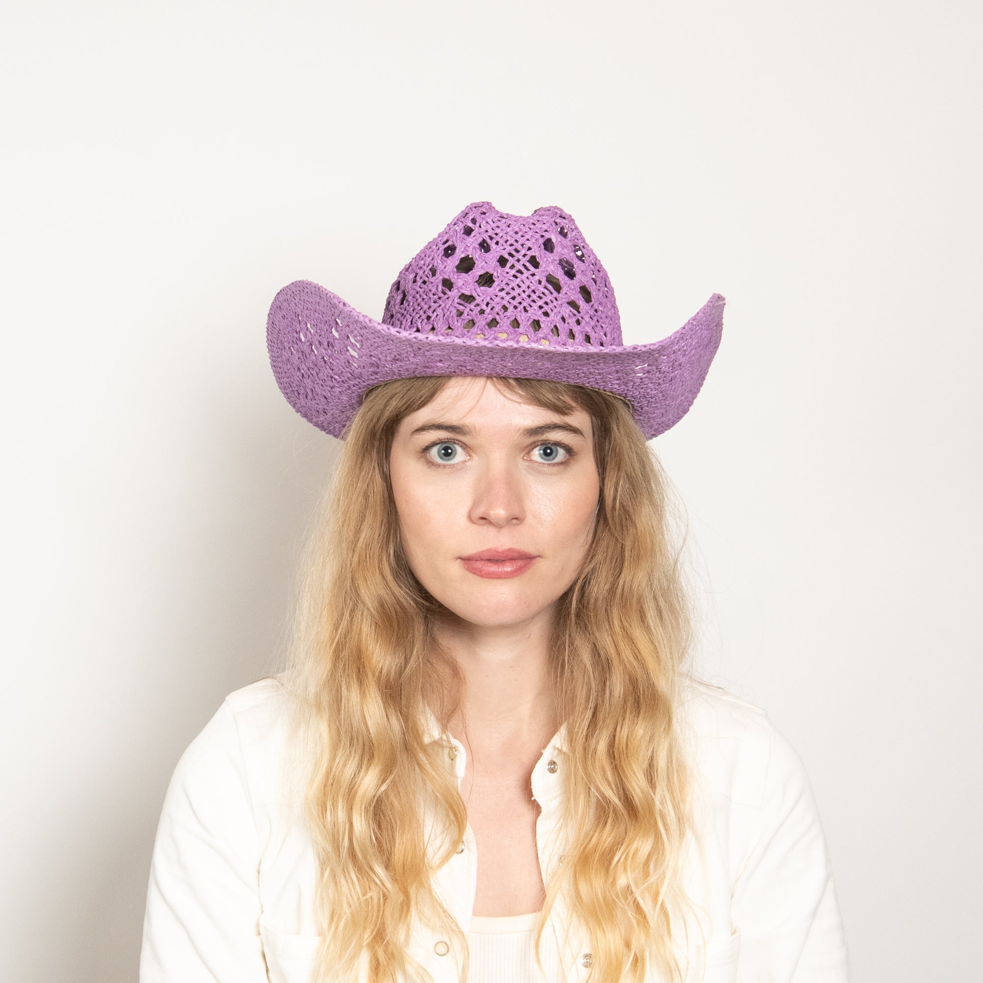 Woman wearing a purple cowboy hat against a plain background