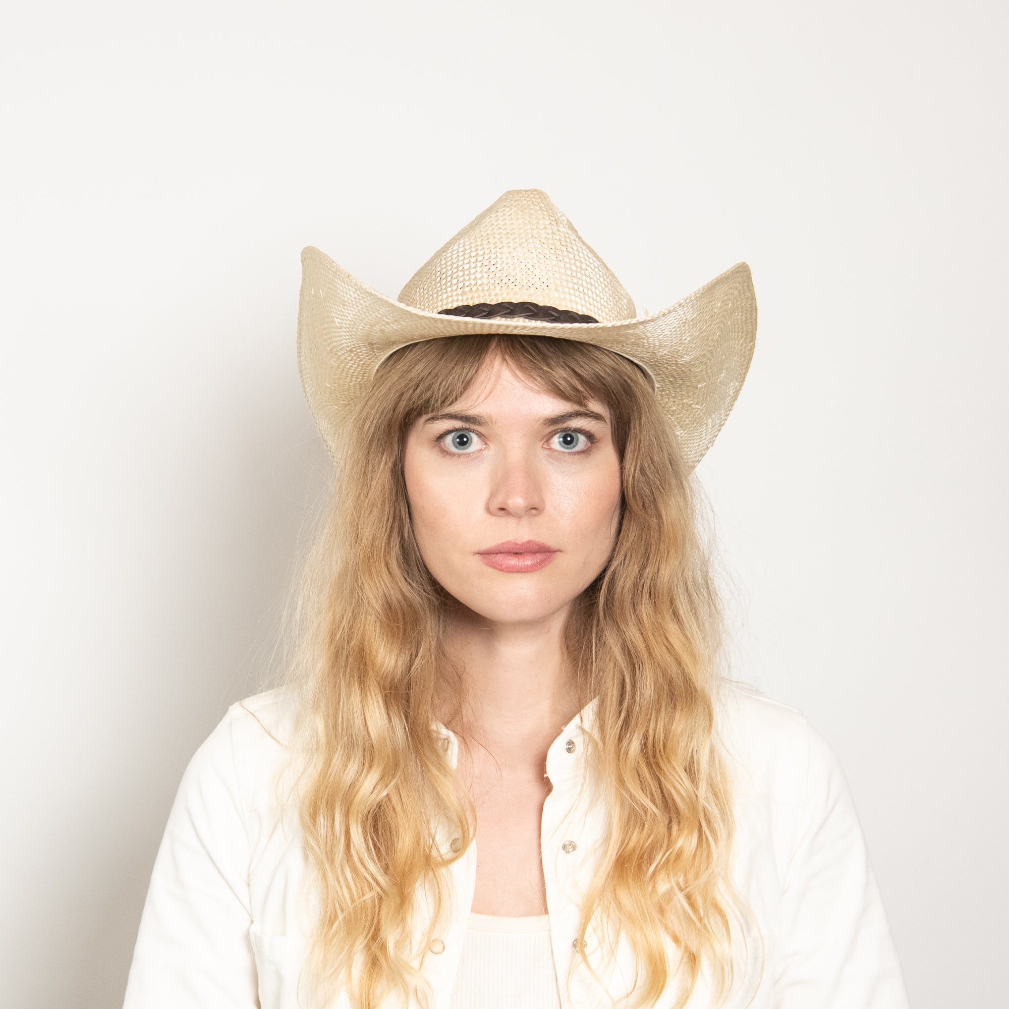 Woman wearing a straw cowboy hat against a plain background
