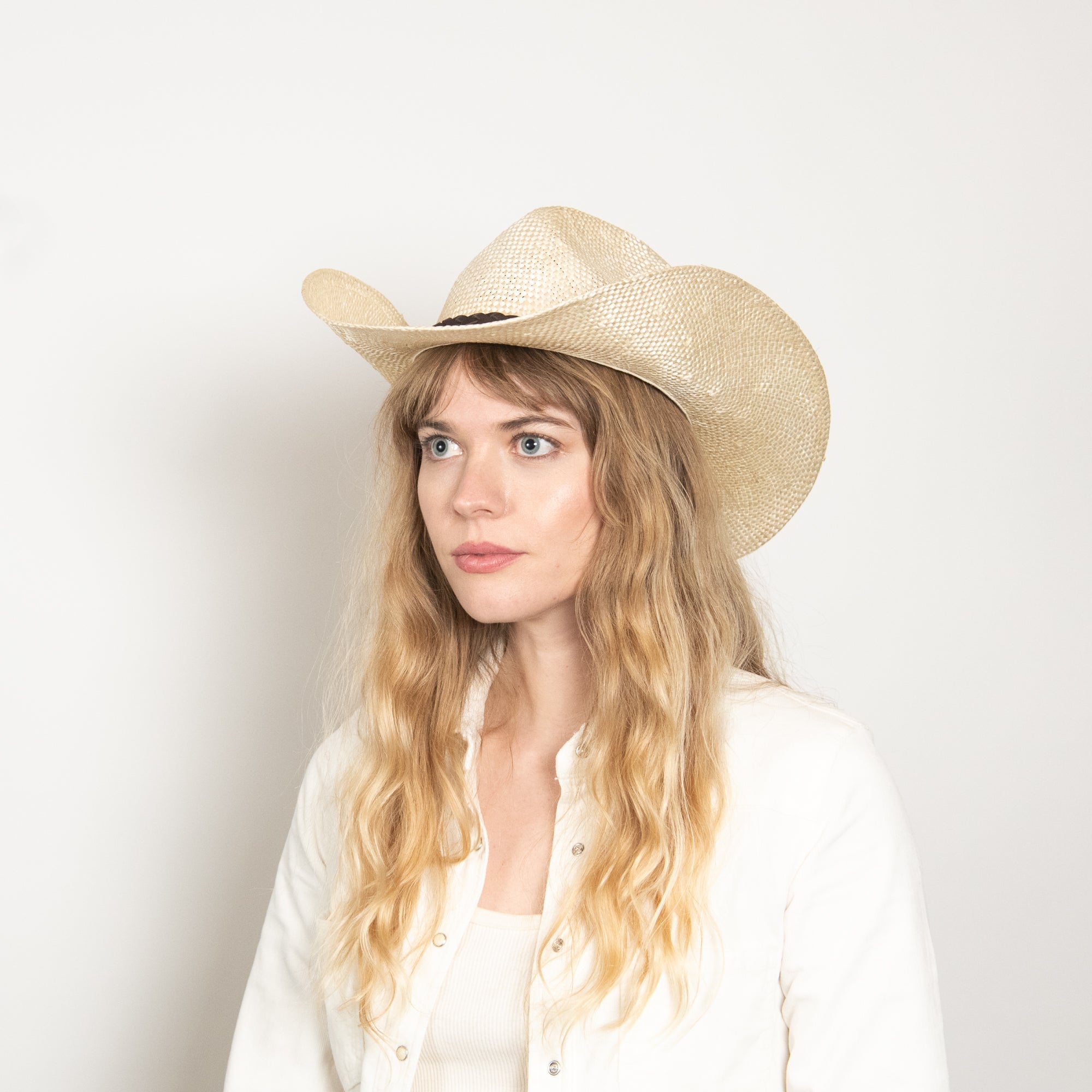 Woman wearing a straw cowboy hat against a plain background