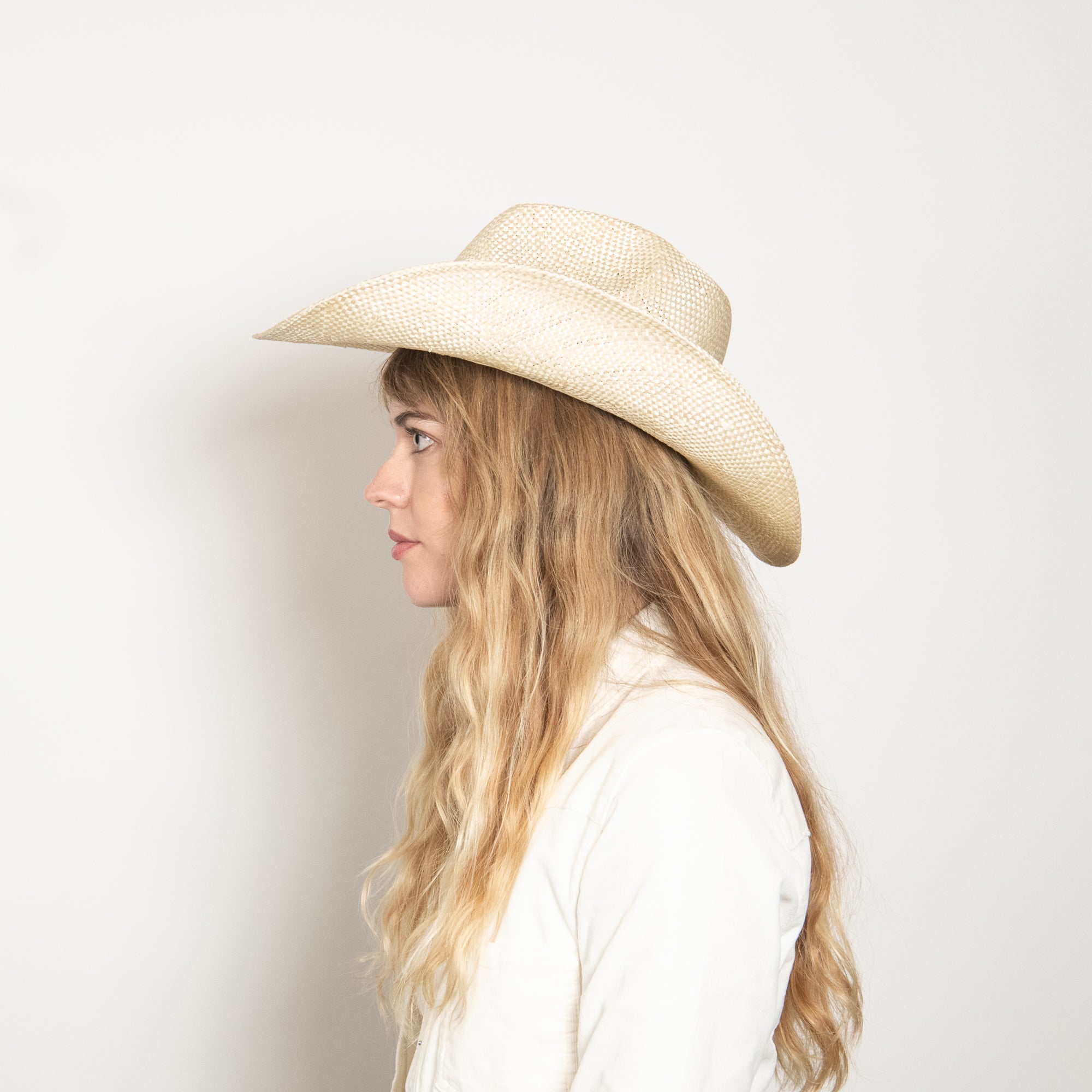 Woman wearing a beige straw hat against a plain background