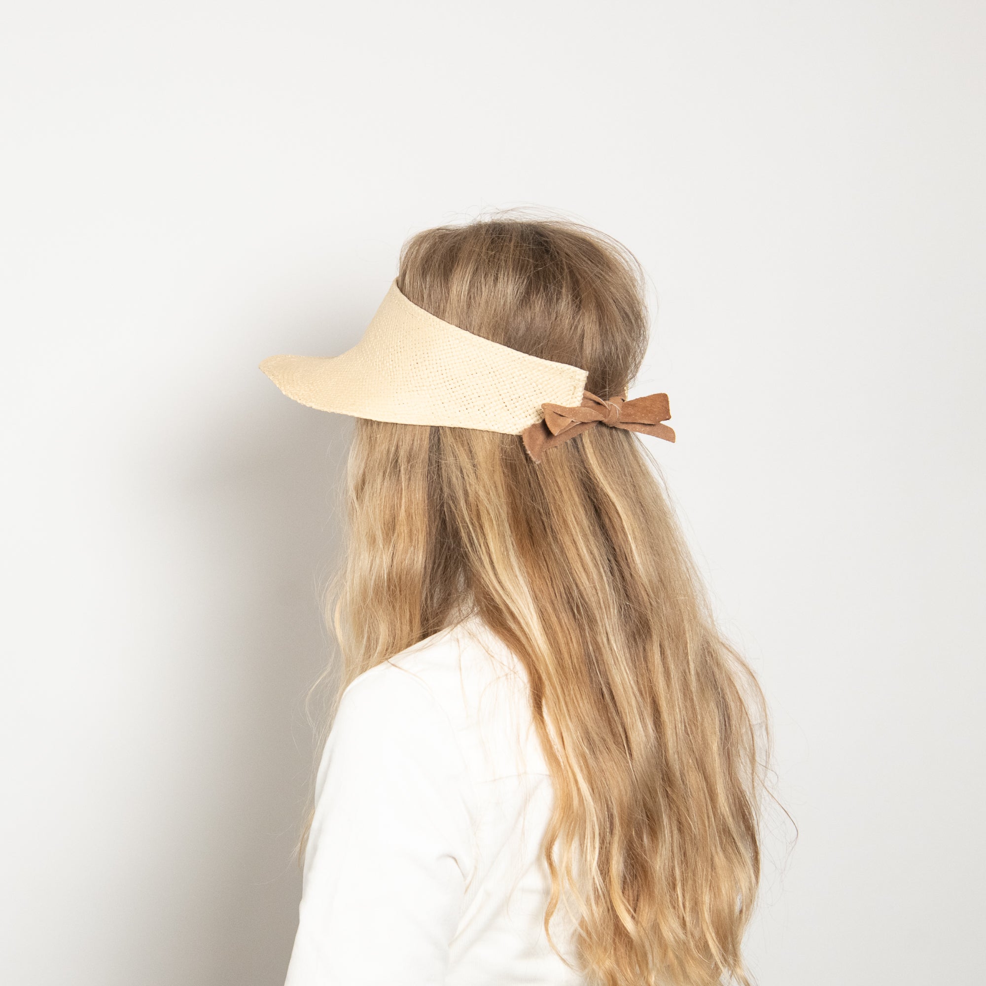 Person wearing a beige visor with a brown bow on a plain background