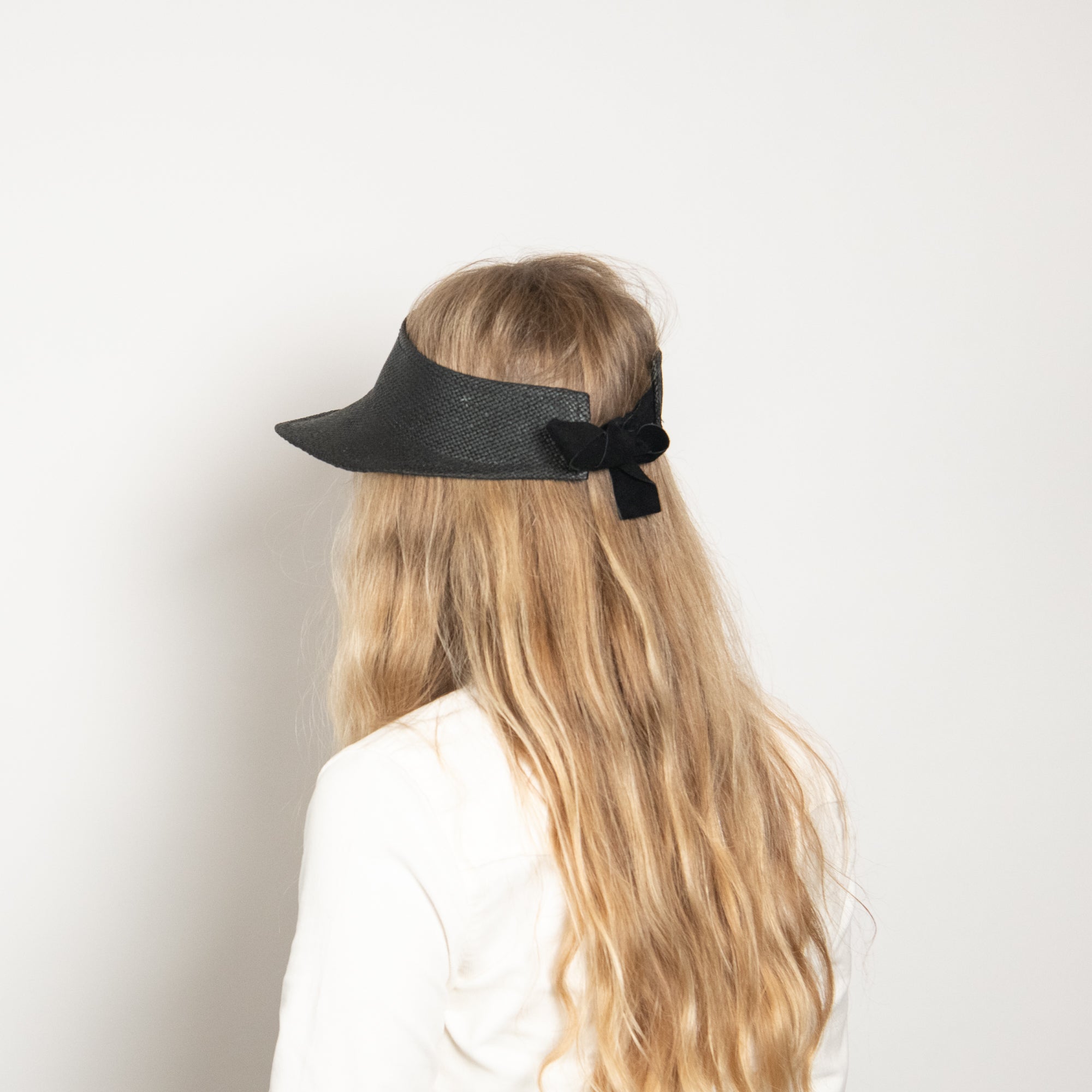 Black visor with a bow on a person with long blonde hair against a white background