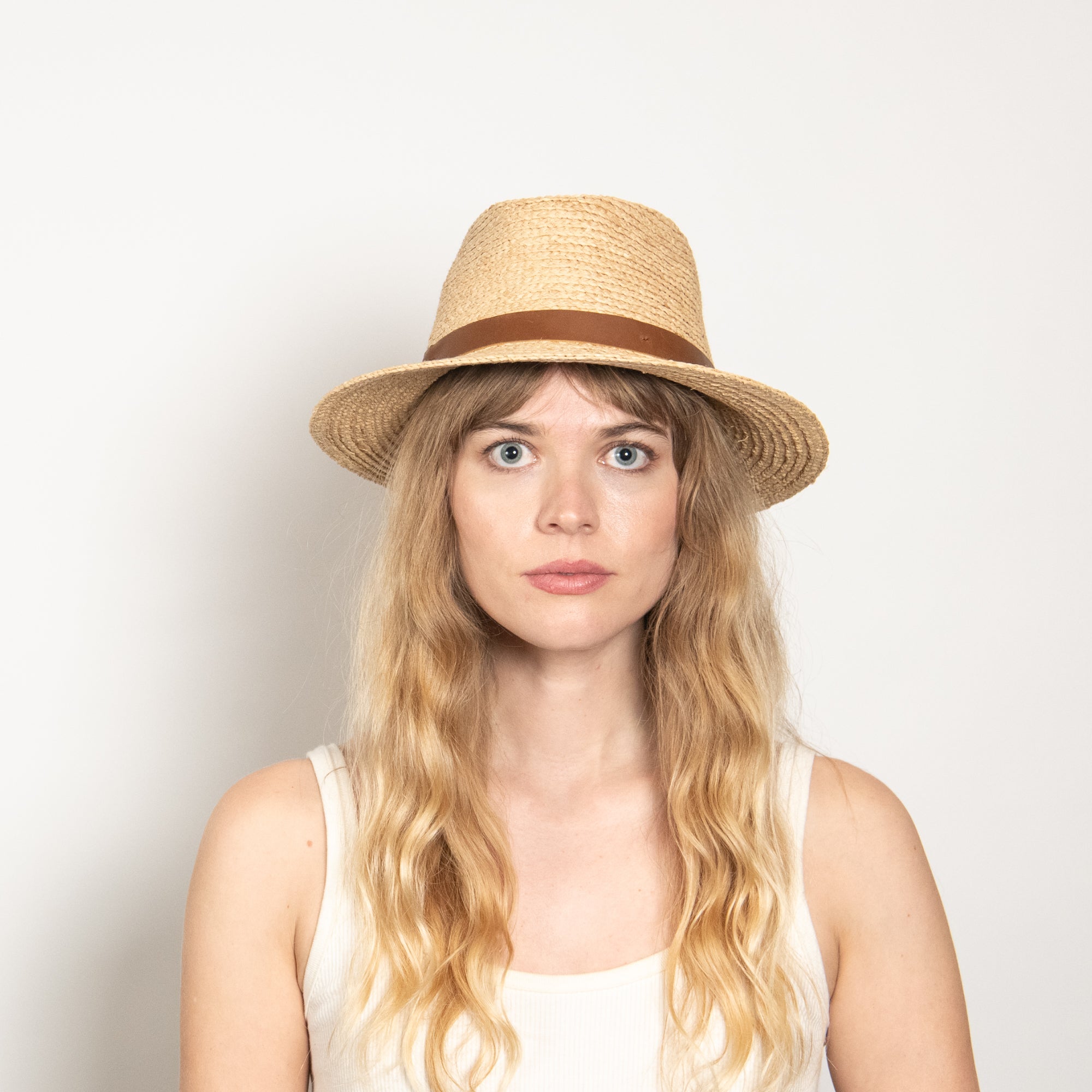 Woman wearing a straw hat with a brown band against a plain background