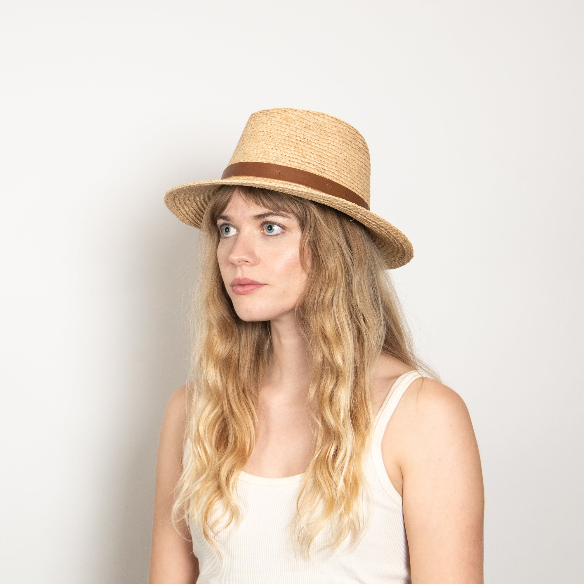 Woman wearing a straw hat with a brown band on a plain background