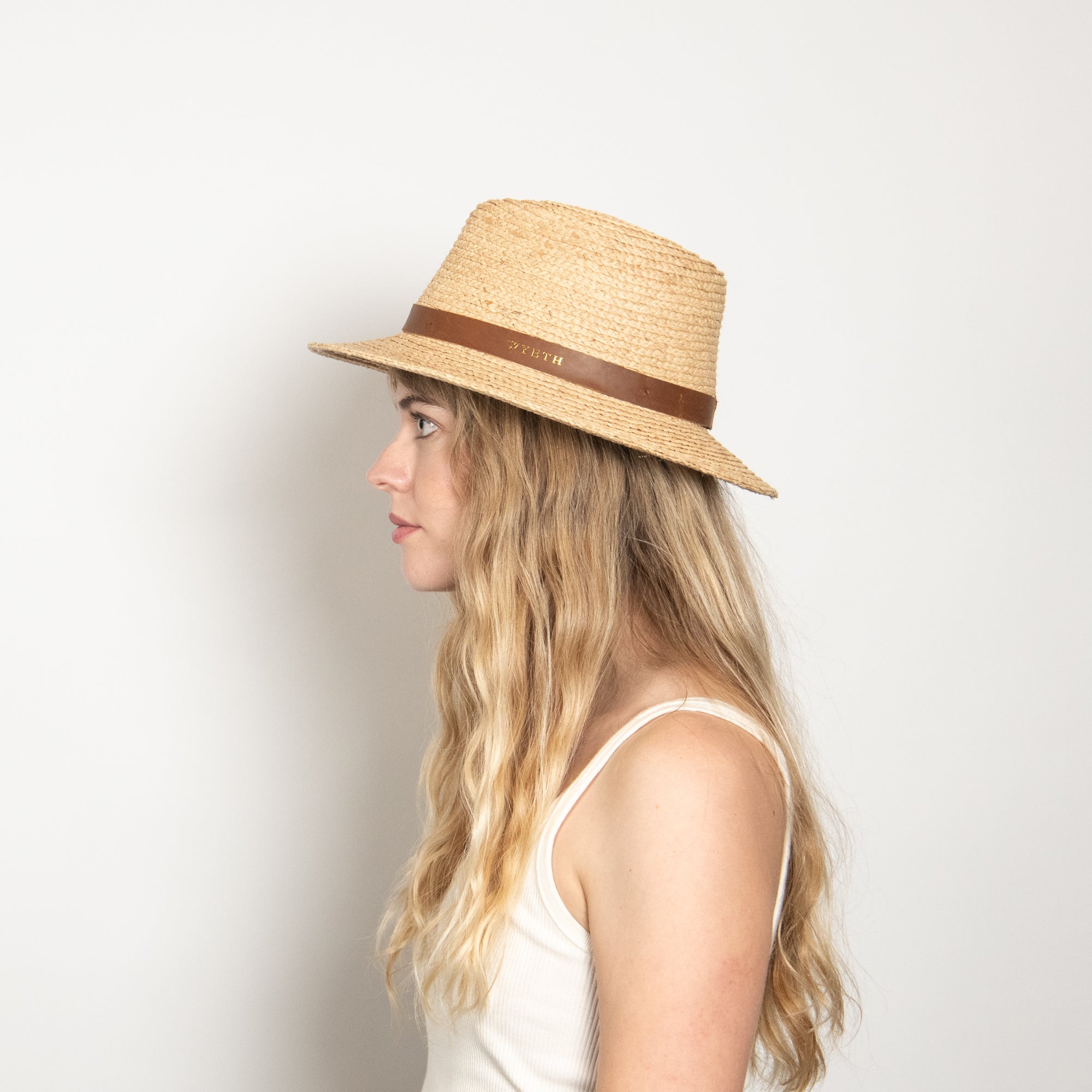 Woman wearing a straw hat with a brown band on a plain background