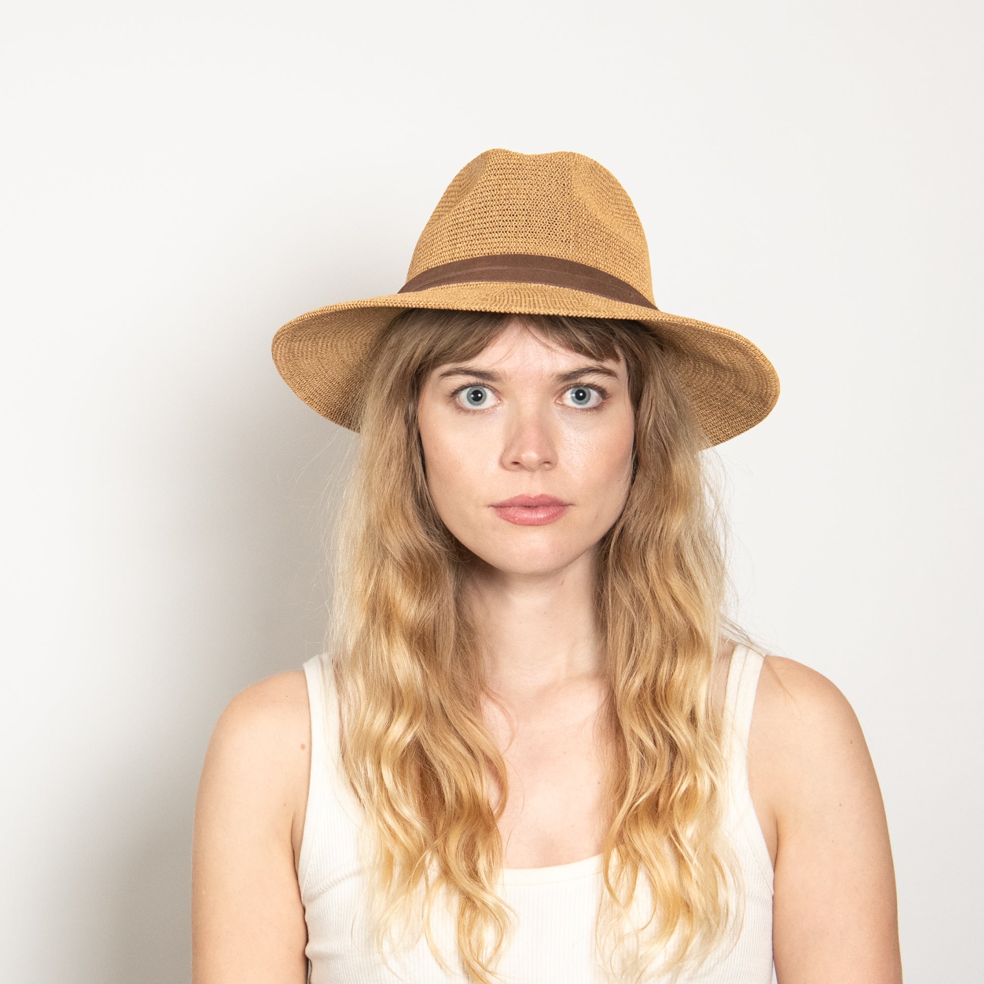 Woman wearing a straw hat with a brown band against a plain background