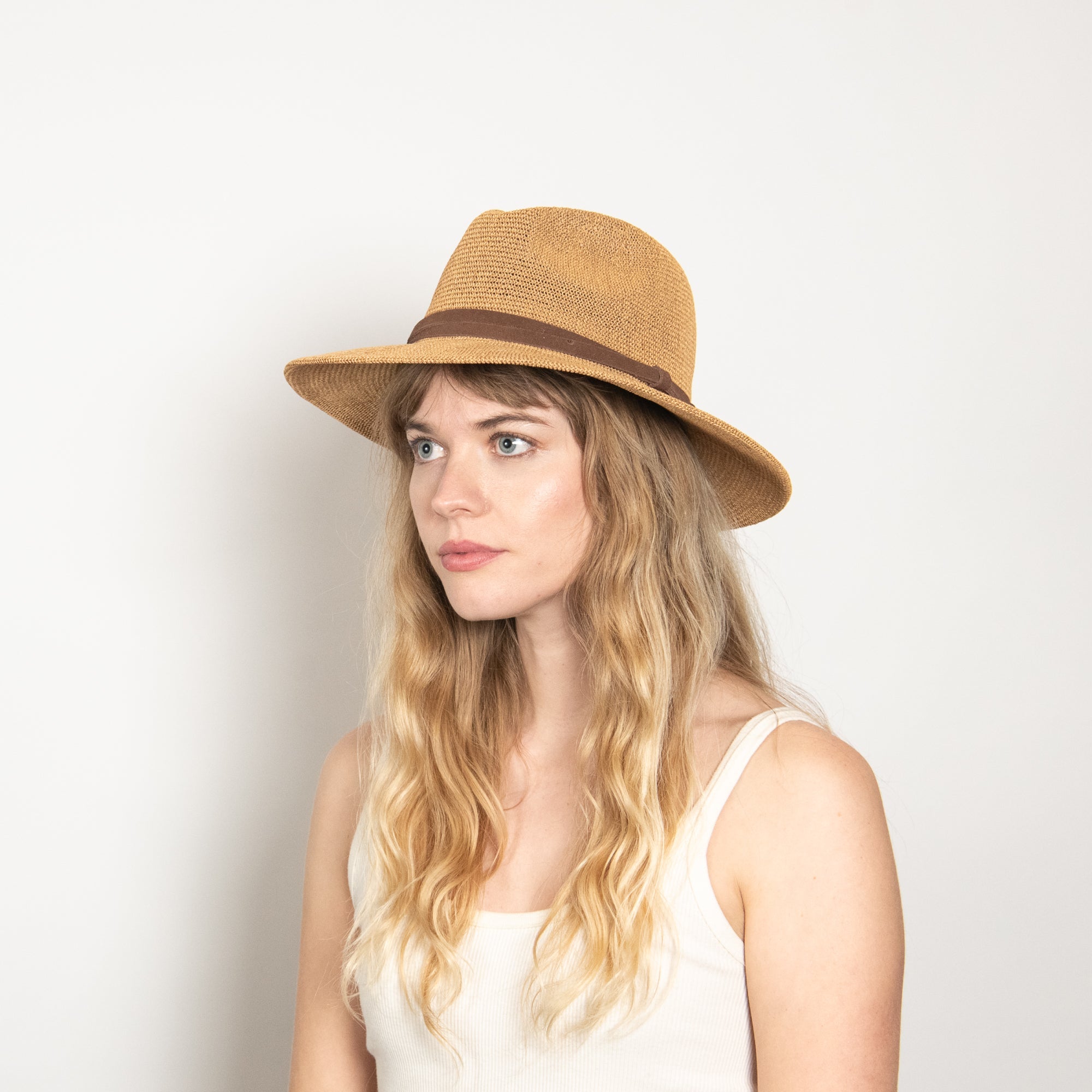 Woman wearing a straw hat with a brown band on a light background