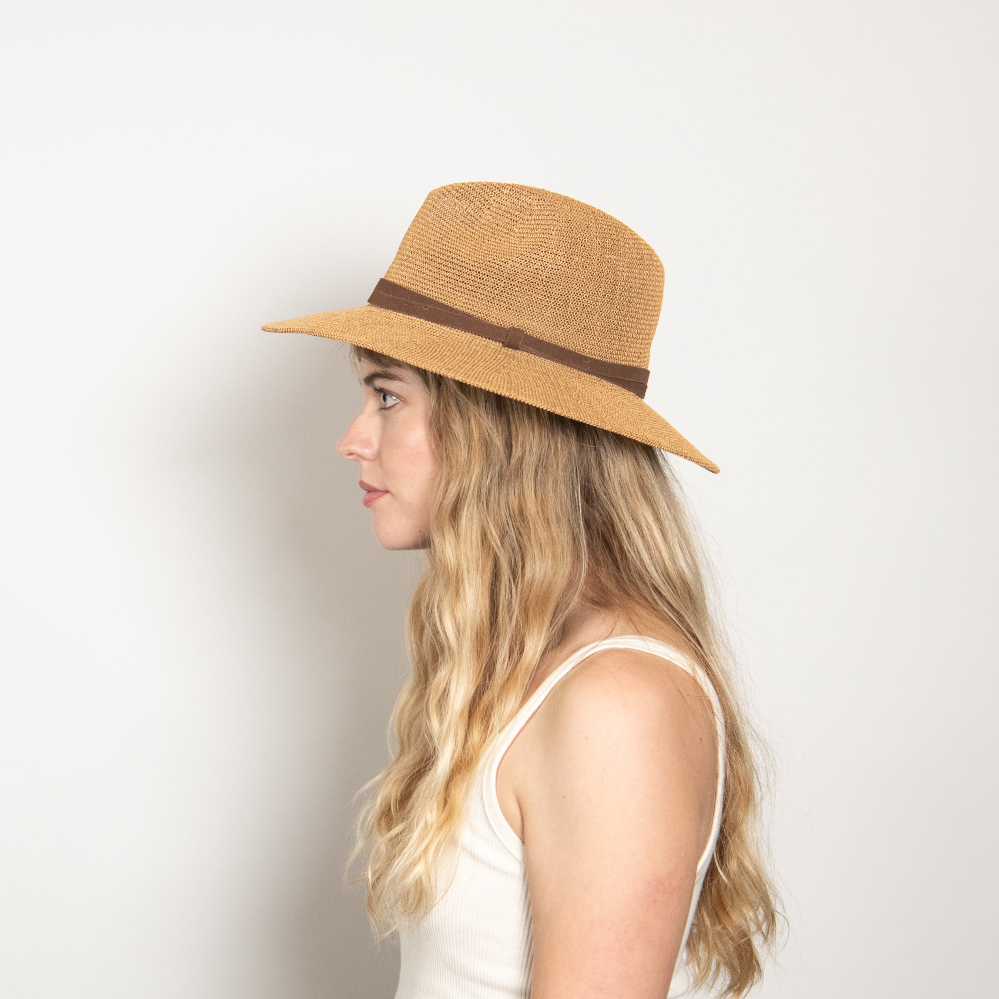 Woman wearing a straw hat with a brown band on a light background
