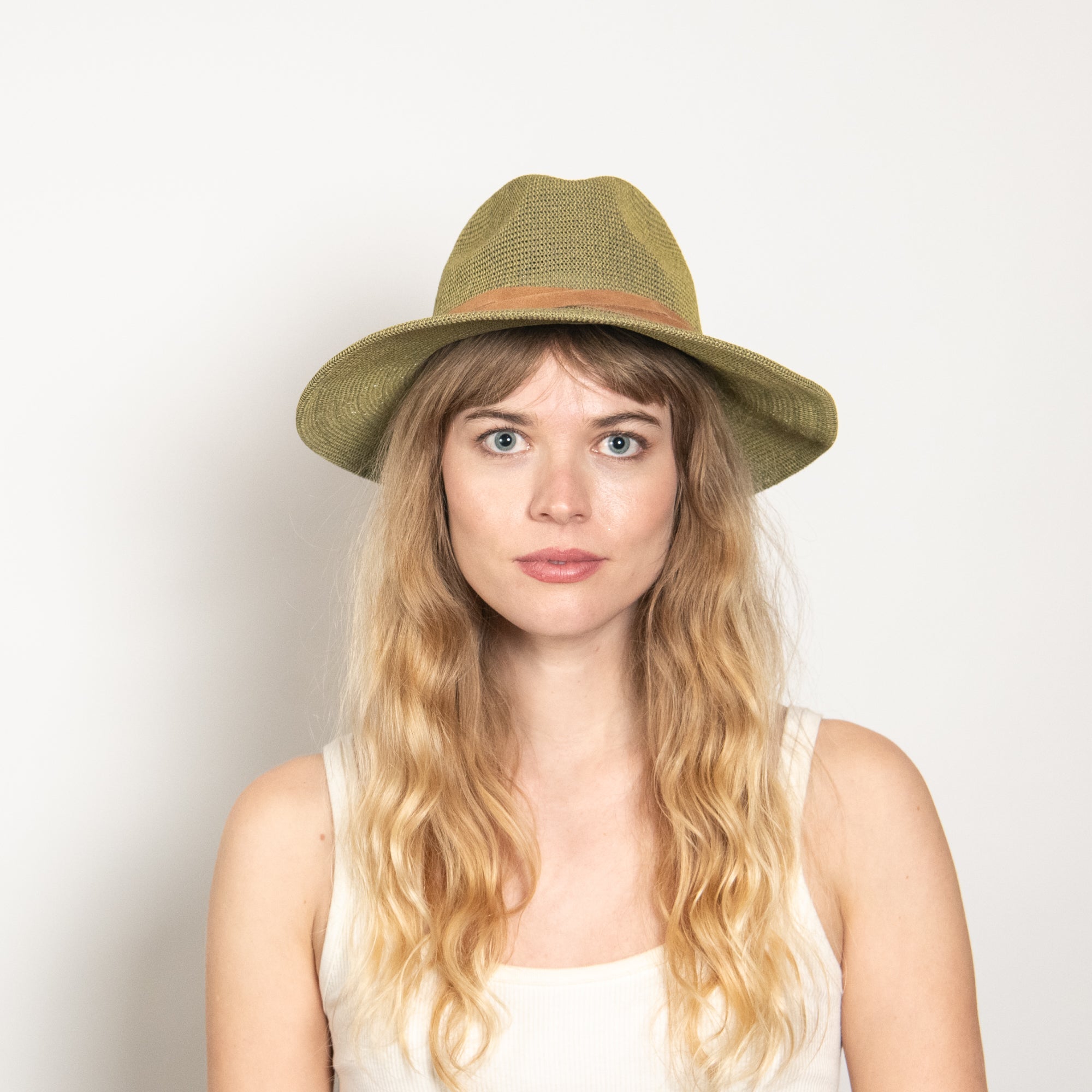 Woman wearing a green straw hat against a plain background